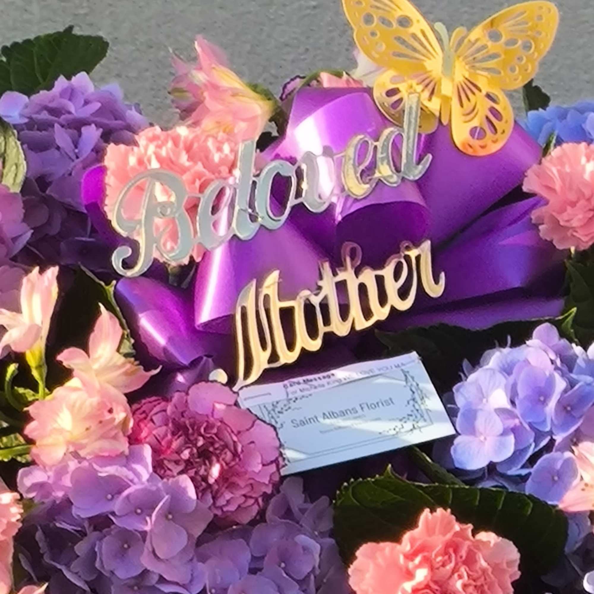 Purple and pink floral arrangement with "Beloved Mother" sign and butterfly decoration