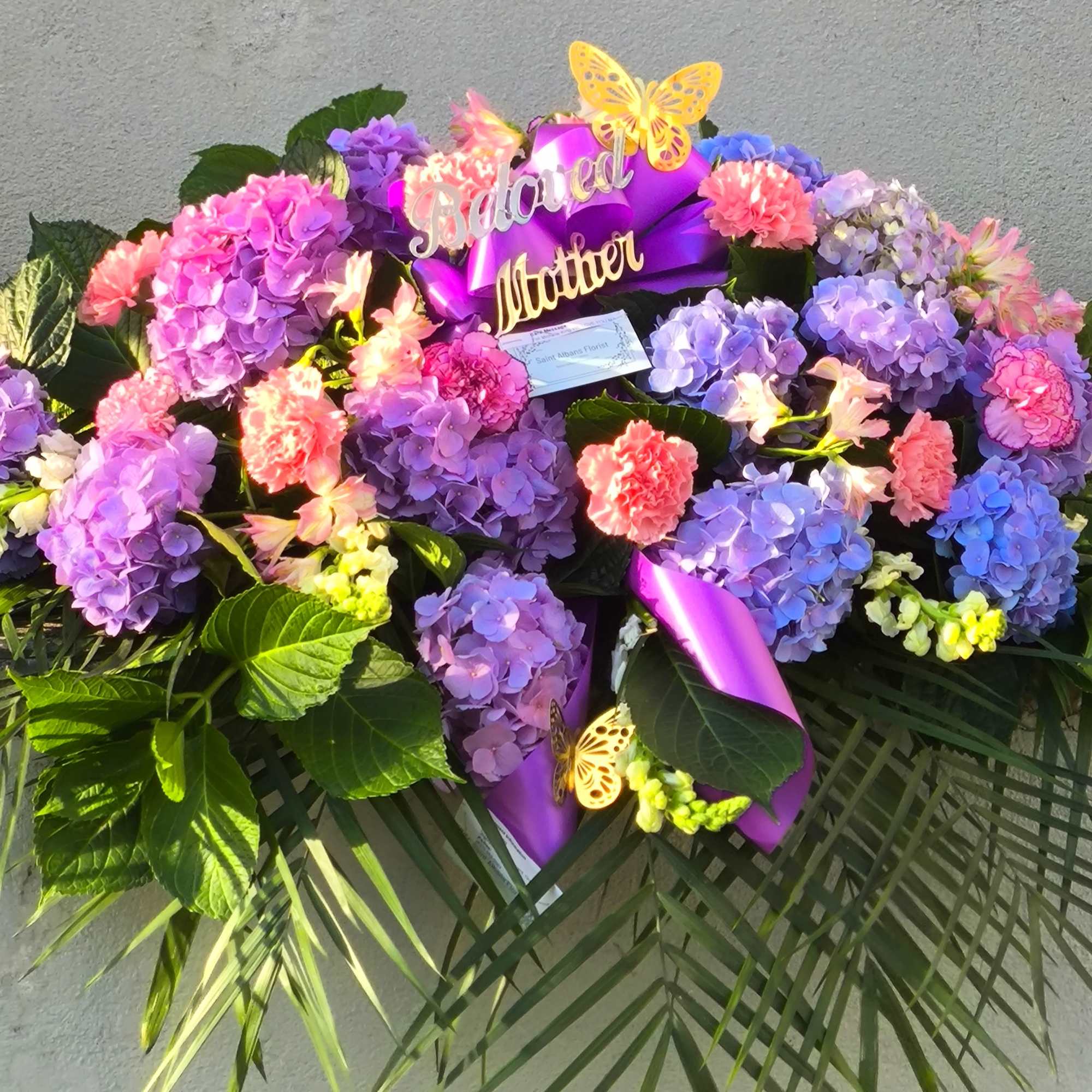 Purple and pink hydrangea arrangement with a "Beloved Mother" sign and butterfly accents