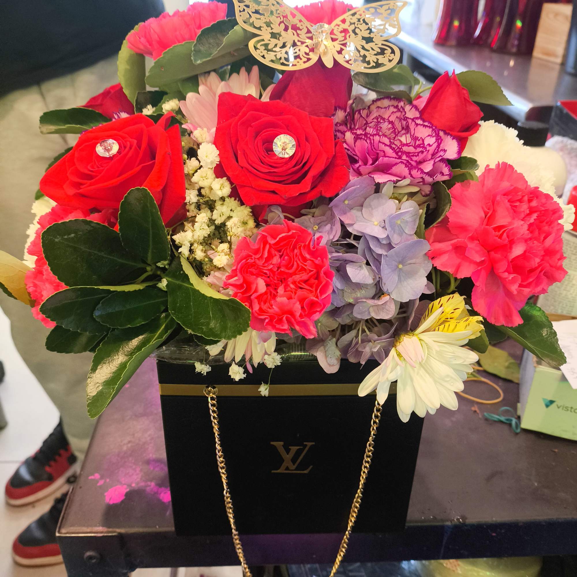 Bright mixed flower arrangement in a black gift box with a gold butterfly topper