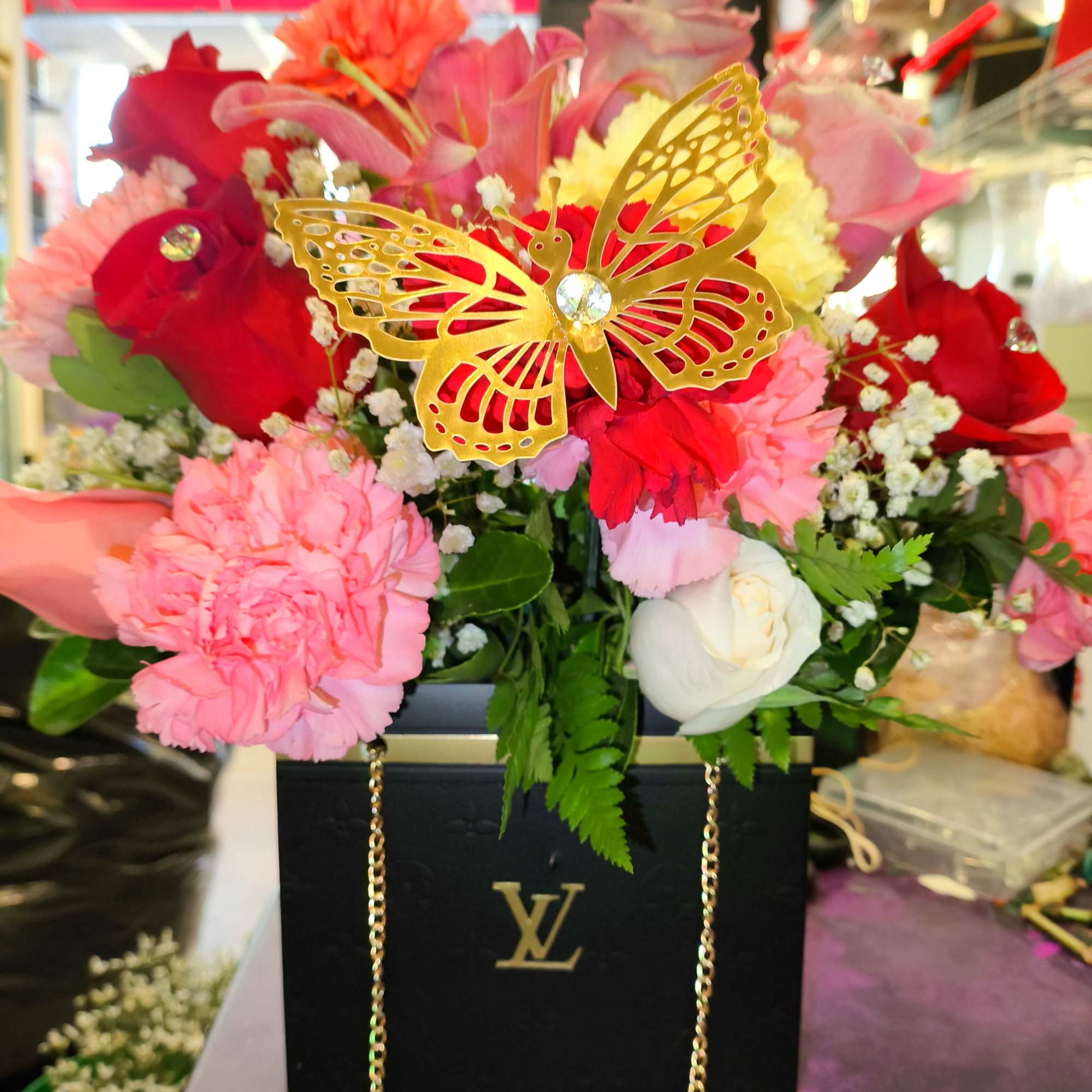 Mixed pink and red flower arrangement in a black box with a gold butterfly