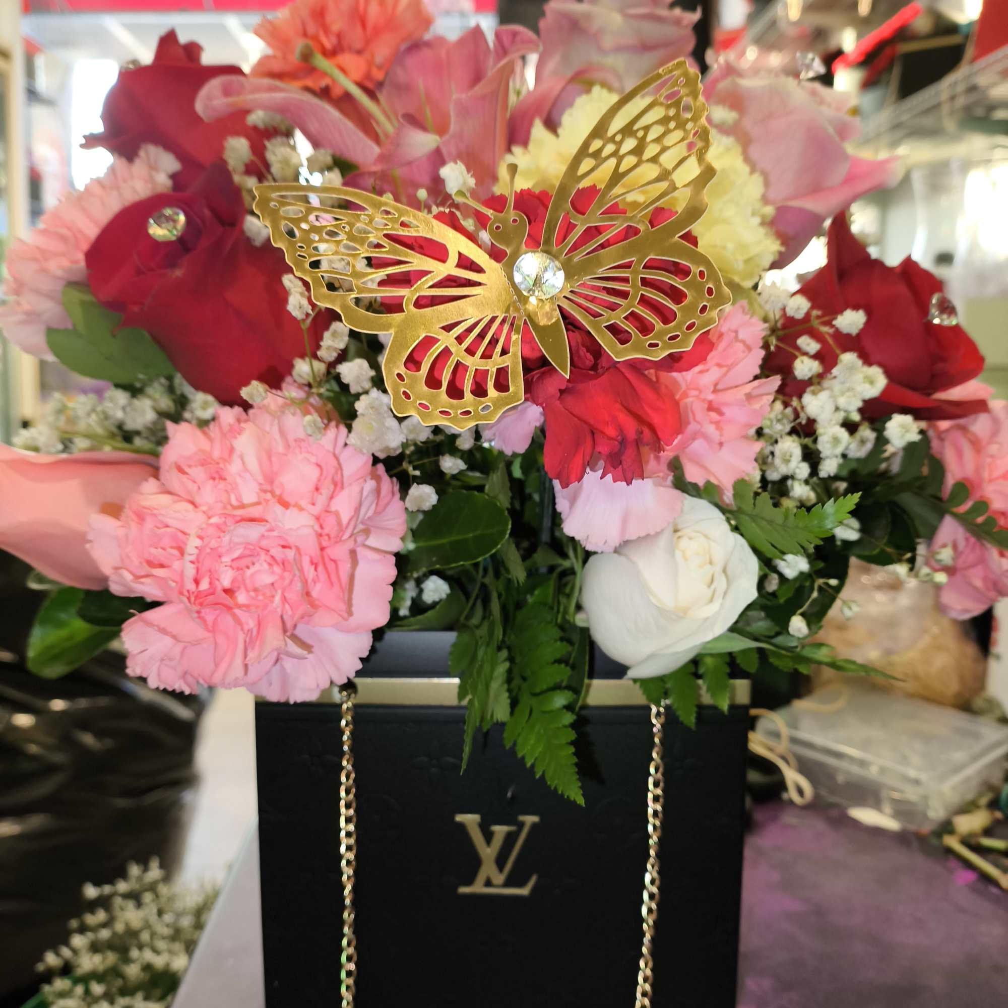 Pink and red flower arrangement in a black box with a gold butterfly decoration