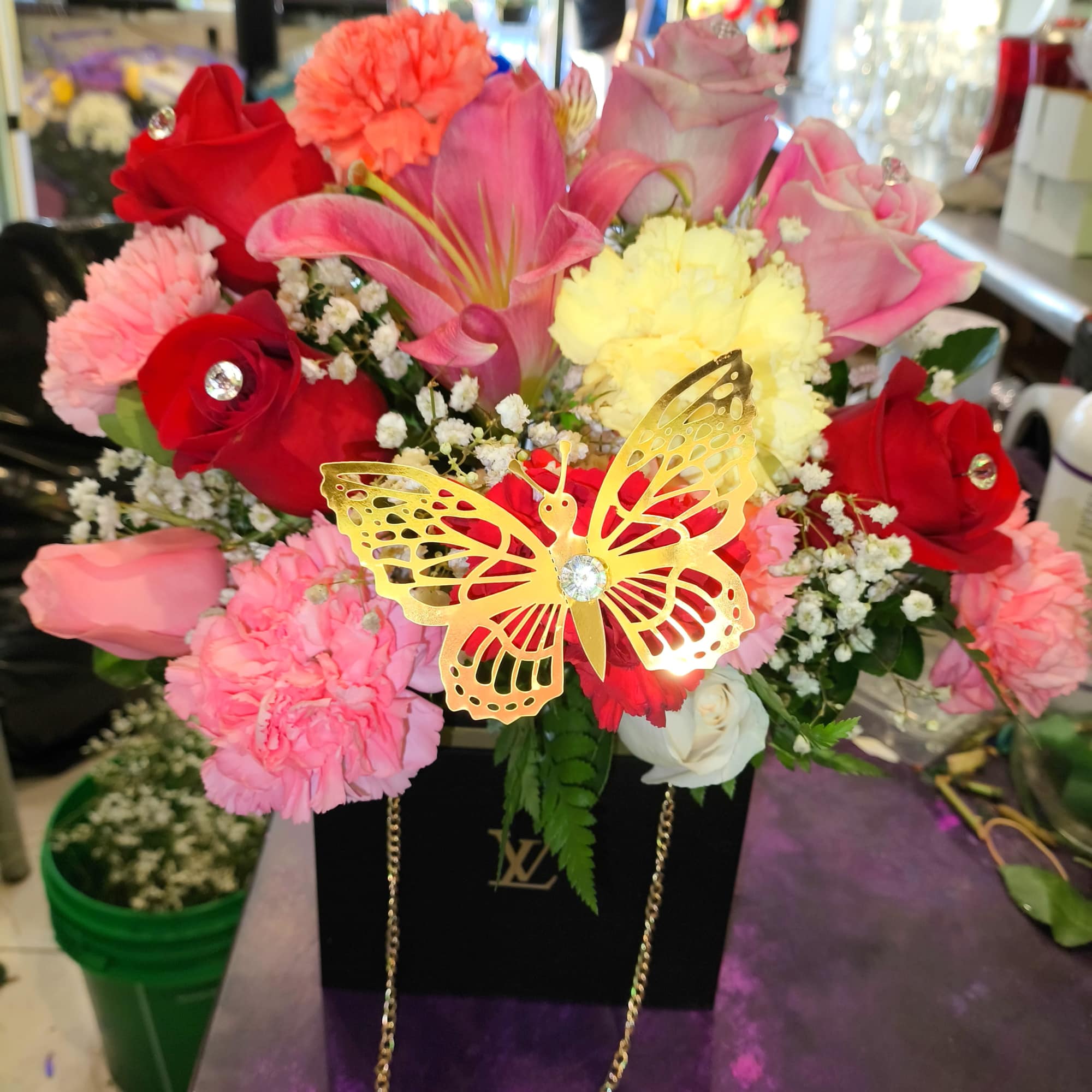Pink and red floral arrangement in a black gift box with a gold butterfly decoration