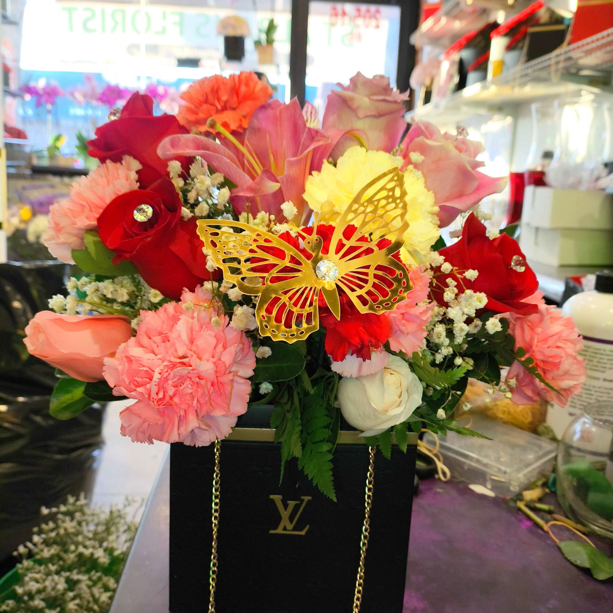 Mixed pink and red flower arrangement in a black gift box with a gold butterfly accent
