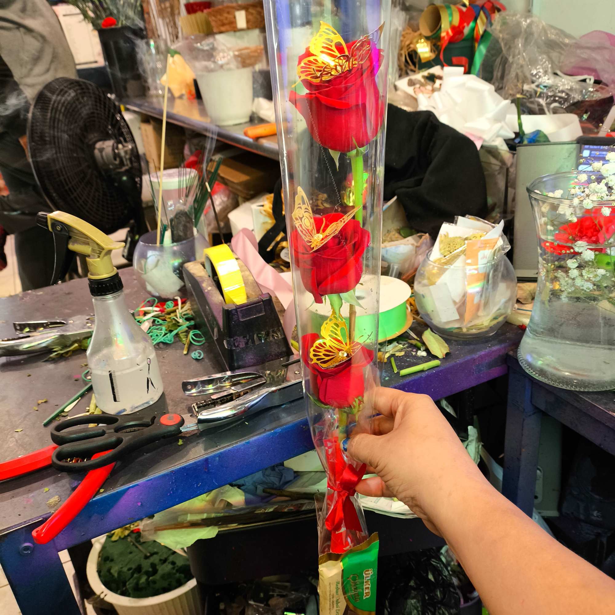 Three red roses in a clear tube with butterfly decorations