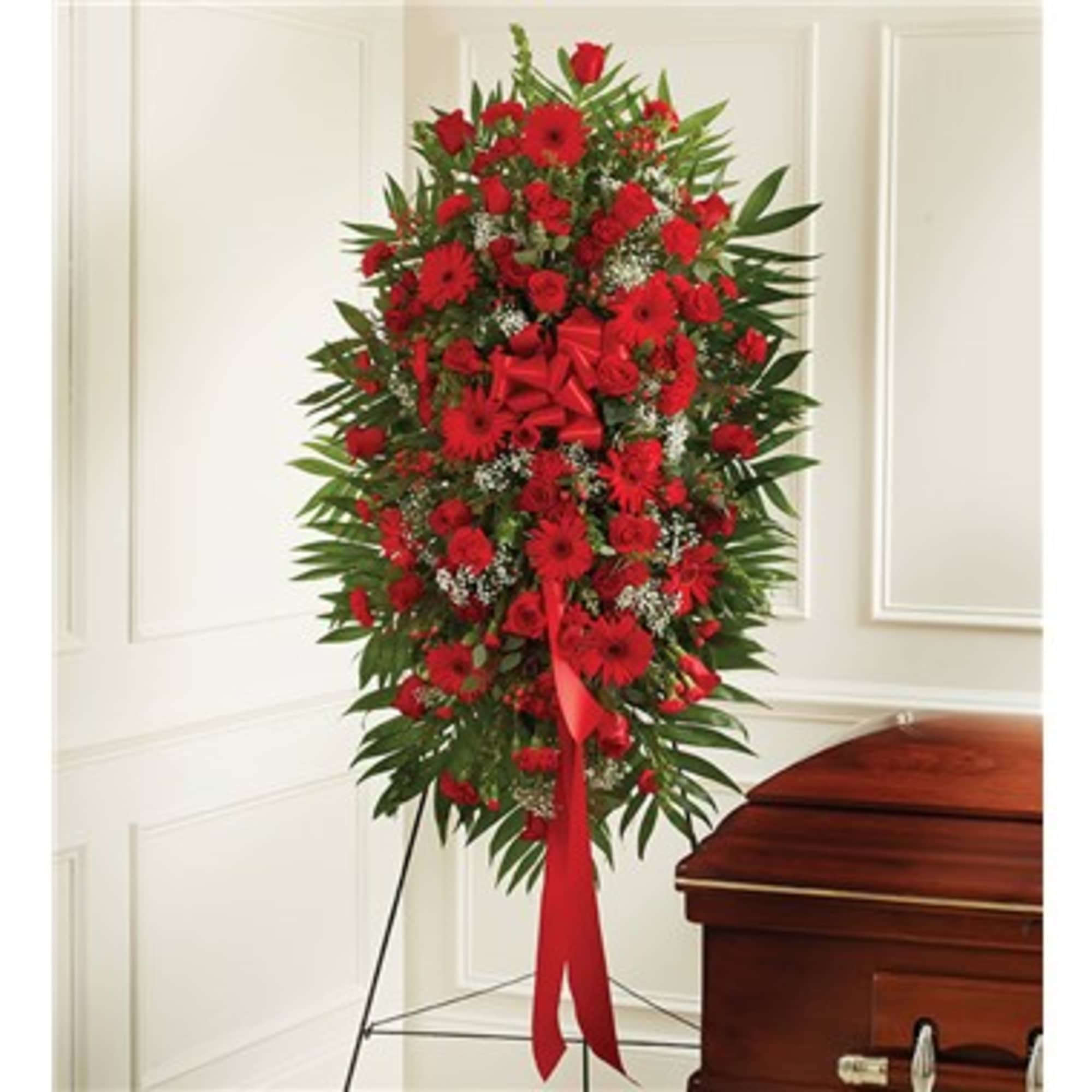Tall red funeral spray with a ribbon on a stand beside a casket