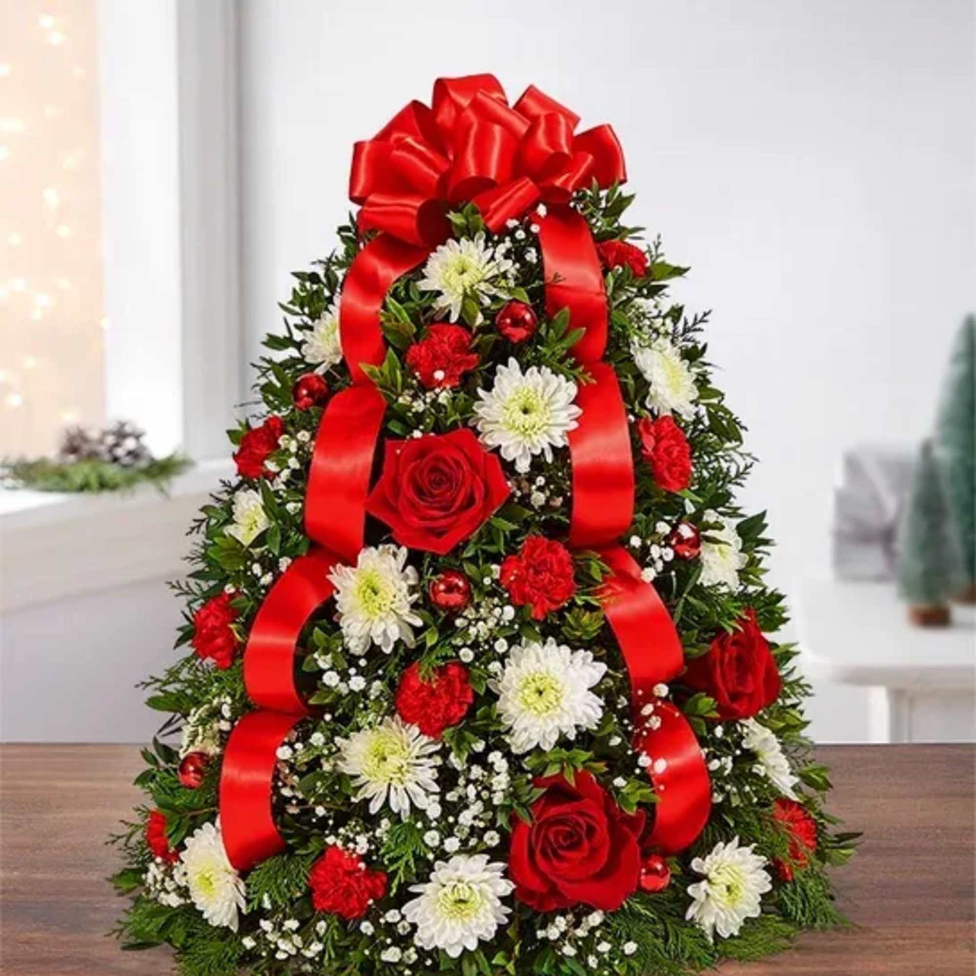 Christmas tree-shaped floral arrangement with red roses, white daisies, and a red ribbon bow