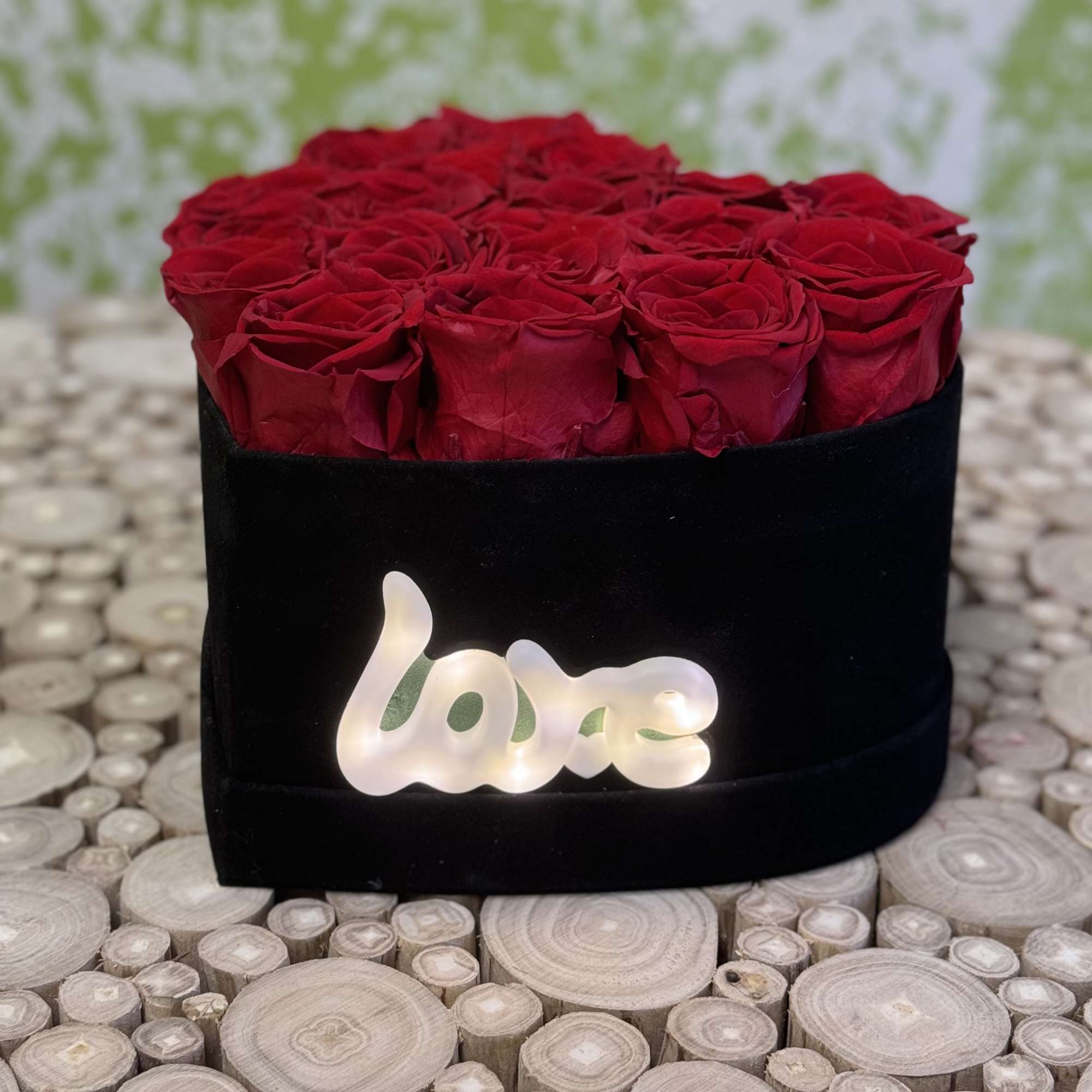 Red roses arranged in a black box with a glowing "love" sign