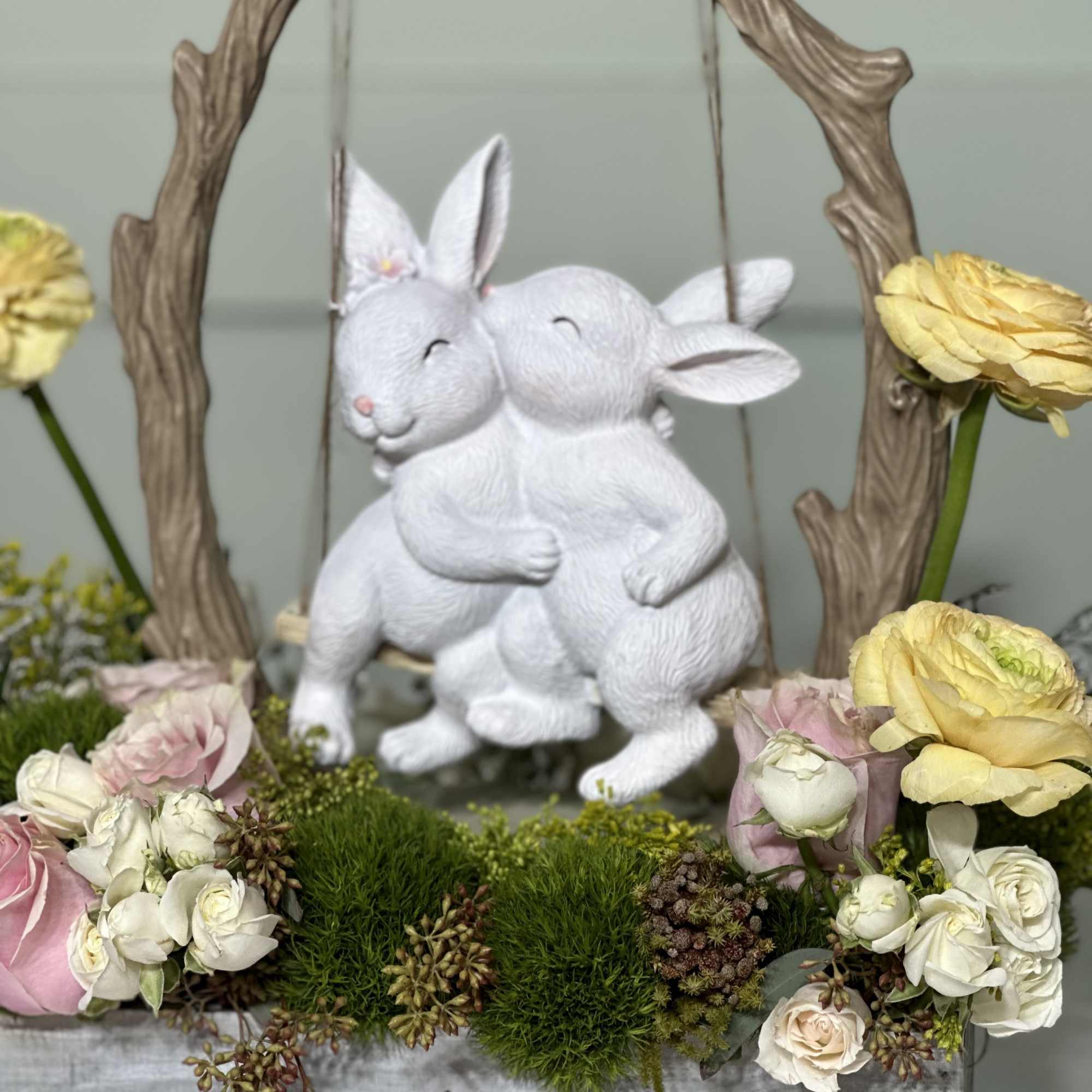 White rabbit figurines in a floral display with pink and yellow roses