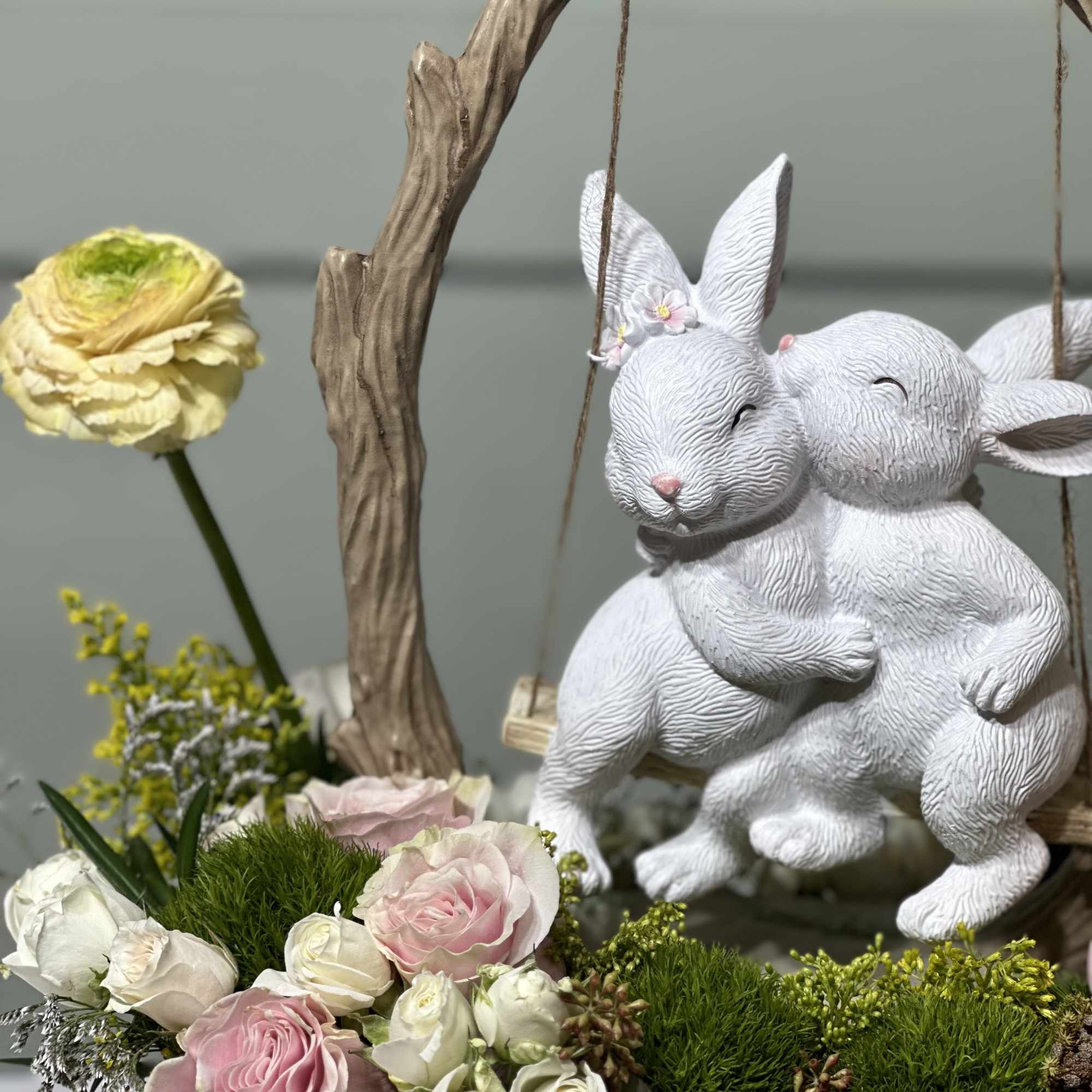 Floral arrangement with pink and white roses beside a white rabbit figurine swing