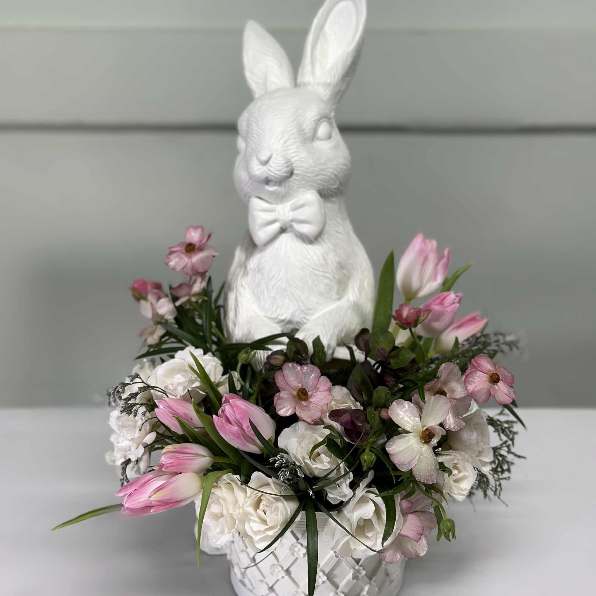White bunny figurine in a flower basket with pink and white tulips