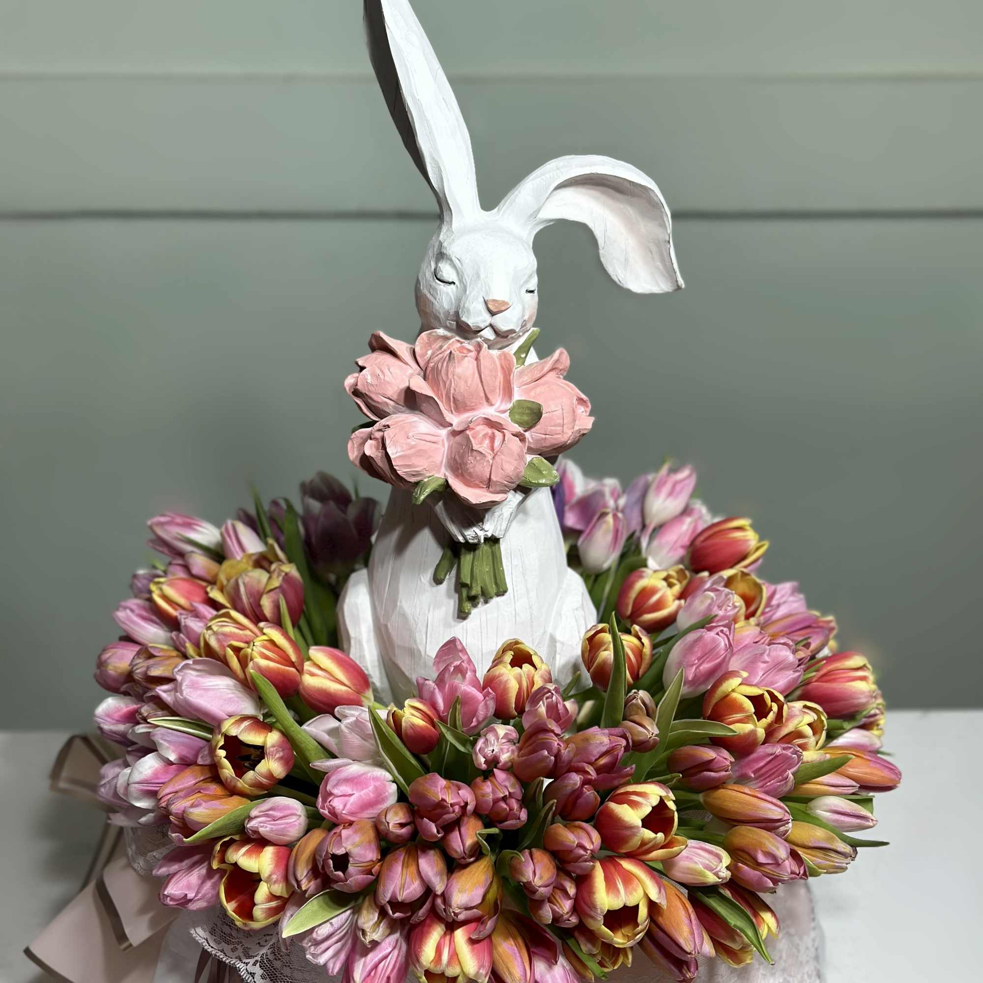 White rabbit figurine holding pink flowers, surrounded by a ring of pink and yellow tulips