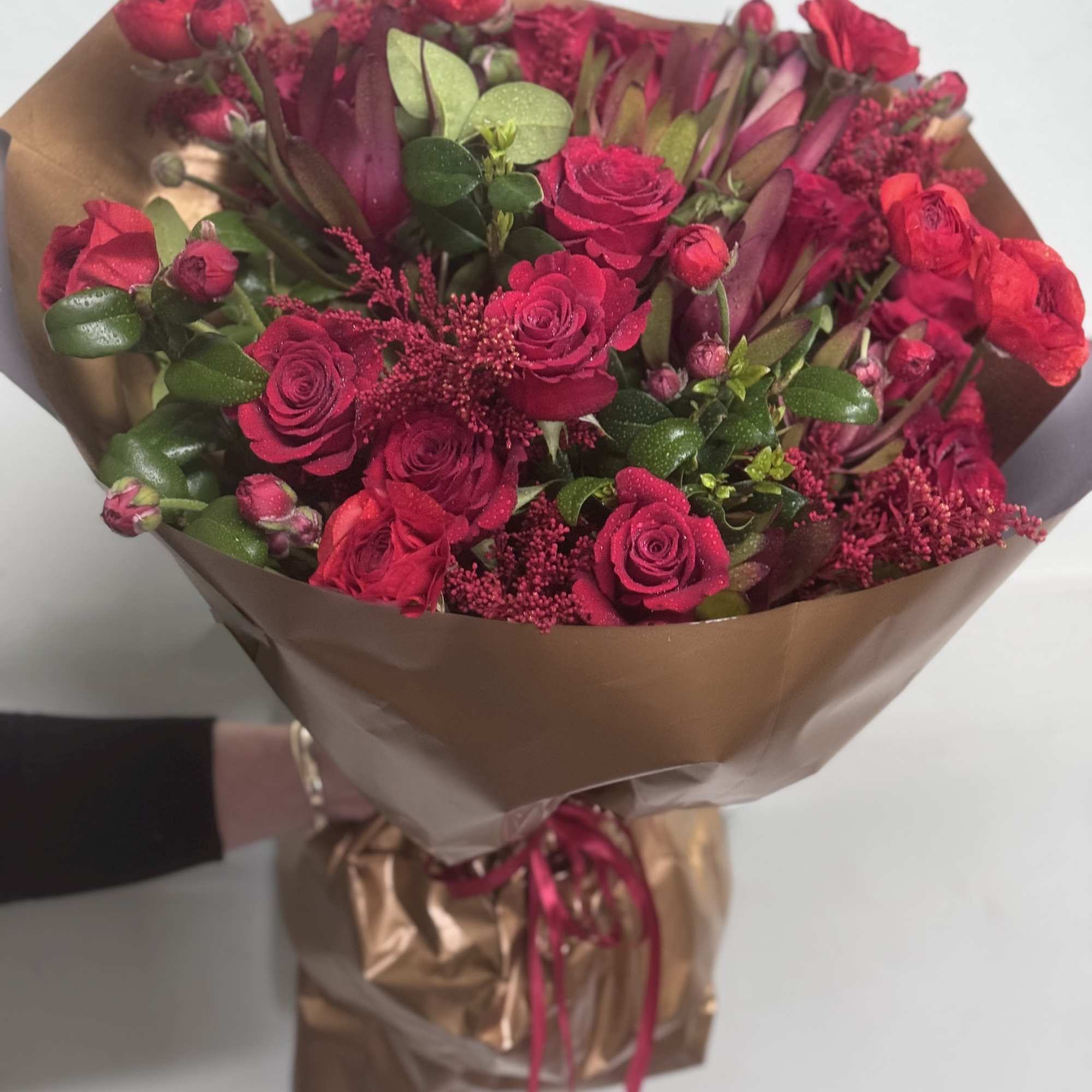 Bouquet of red roses and burgundy flowers wrapped in brown paper