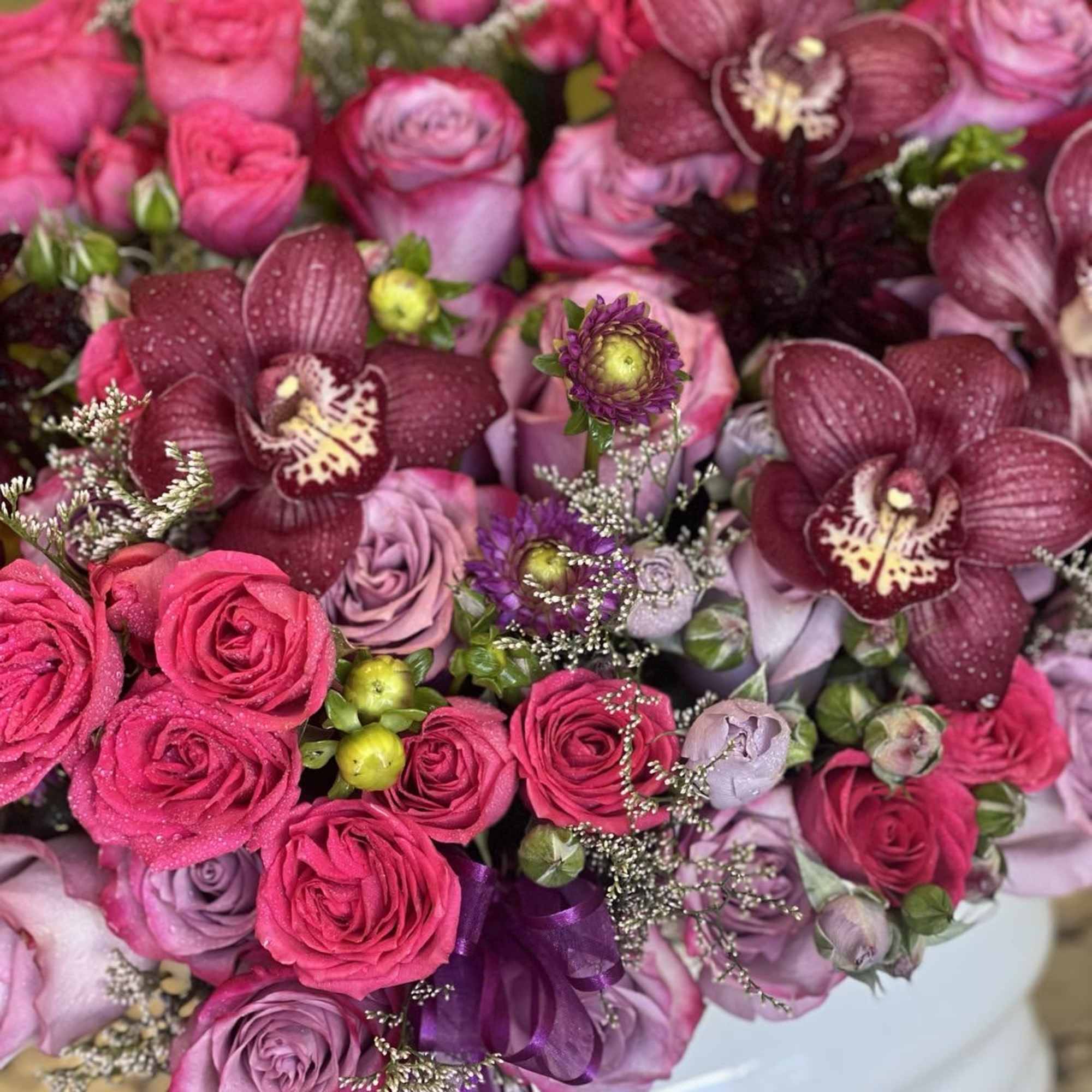 Bouquet of pink and purple roses with dark orchids in a white container