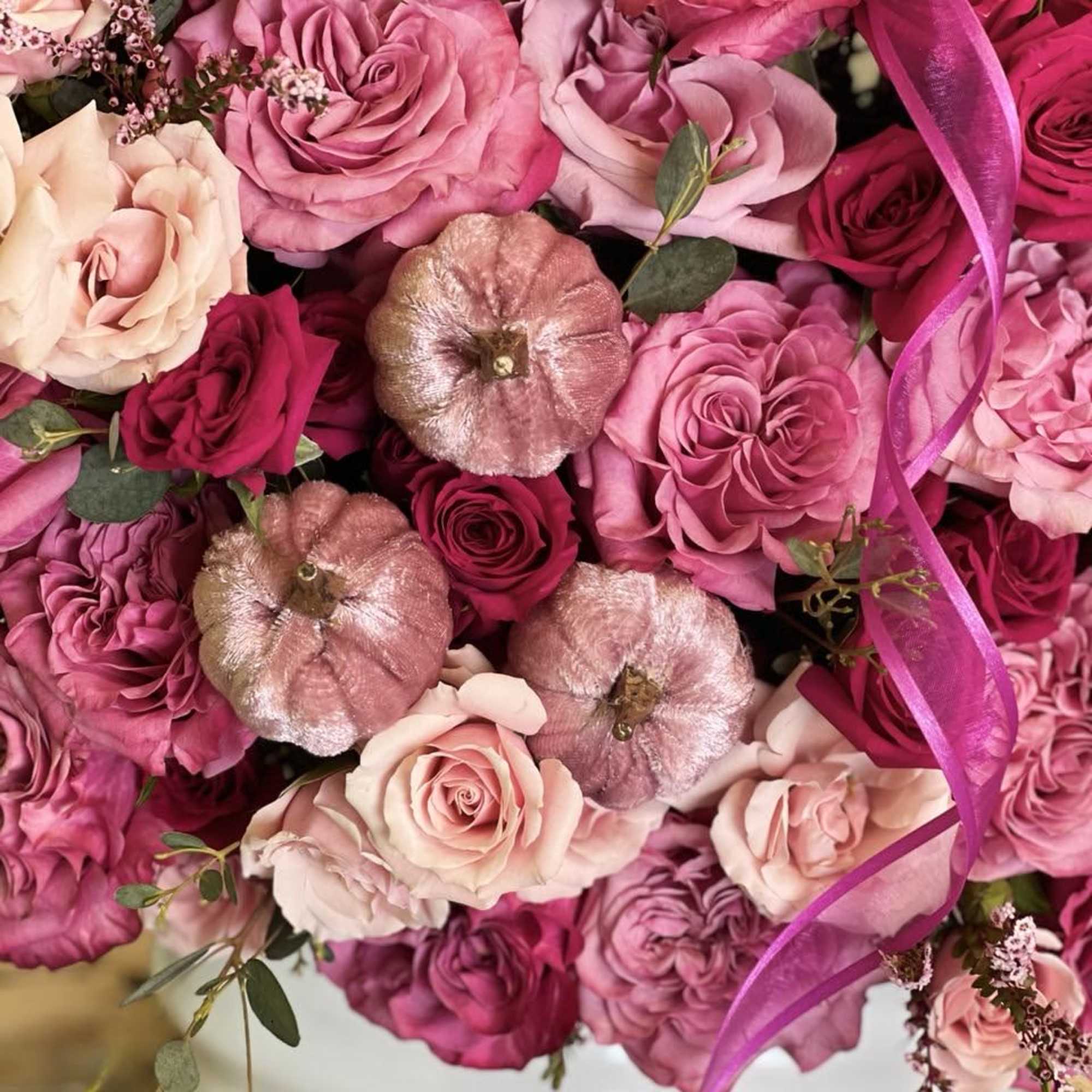 Bouquet of pink and magenta roses with metallic pumpkins in a white vase