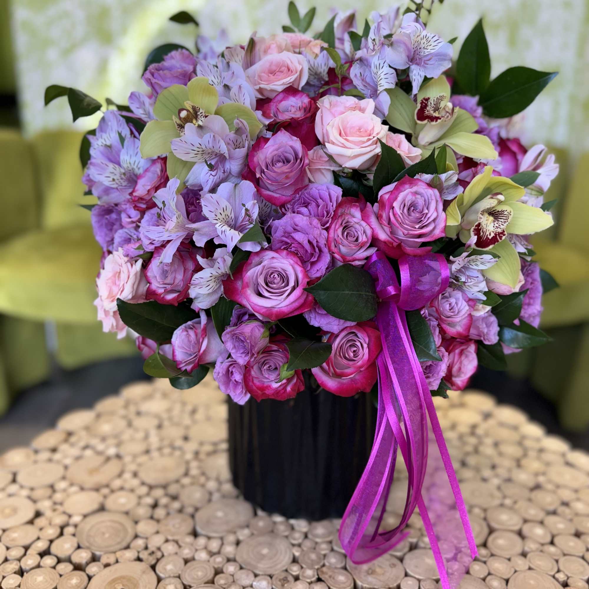 Pink and lavender bouquet of roses and orchids in a black vase with ribbon