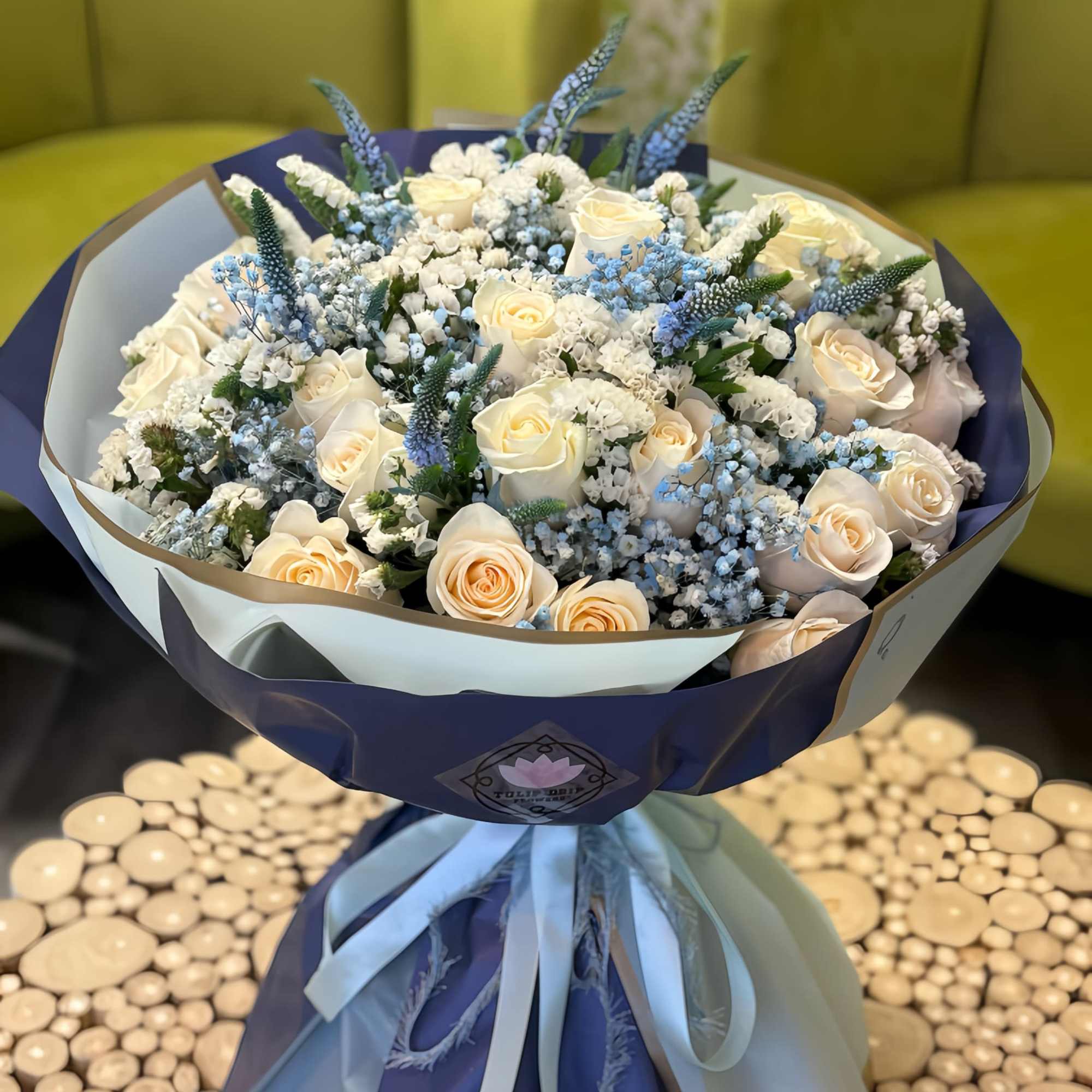 Bouquet of cream roses and blue filler flowers wrapped in navy and white paper