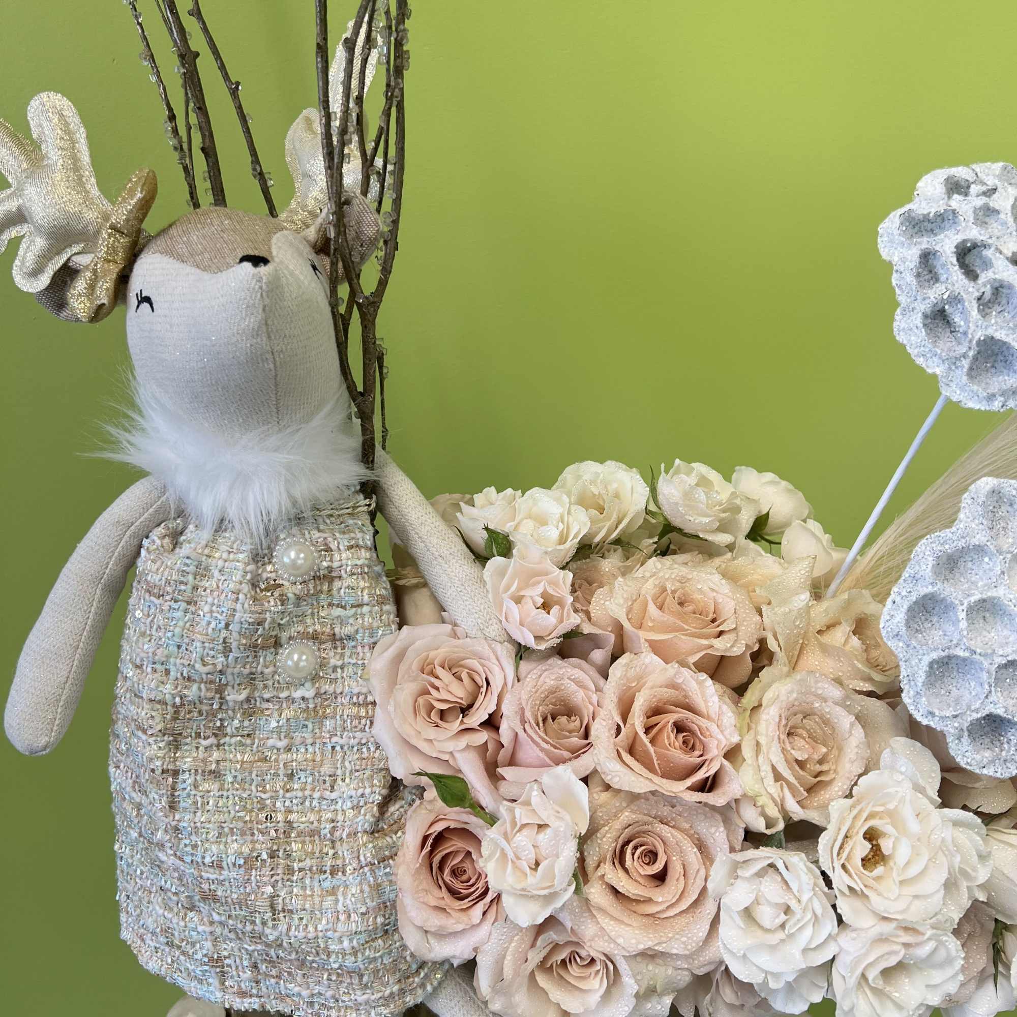 Plush reindeer beside a bouquet of pale roses in a vase.