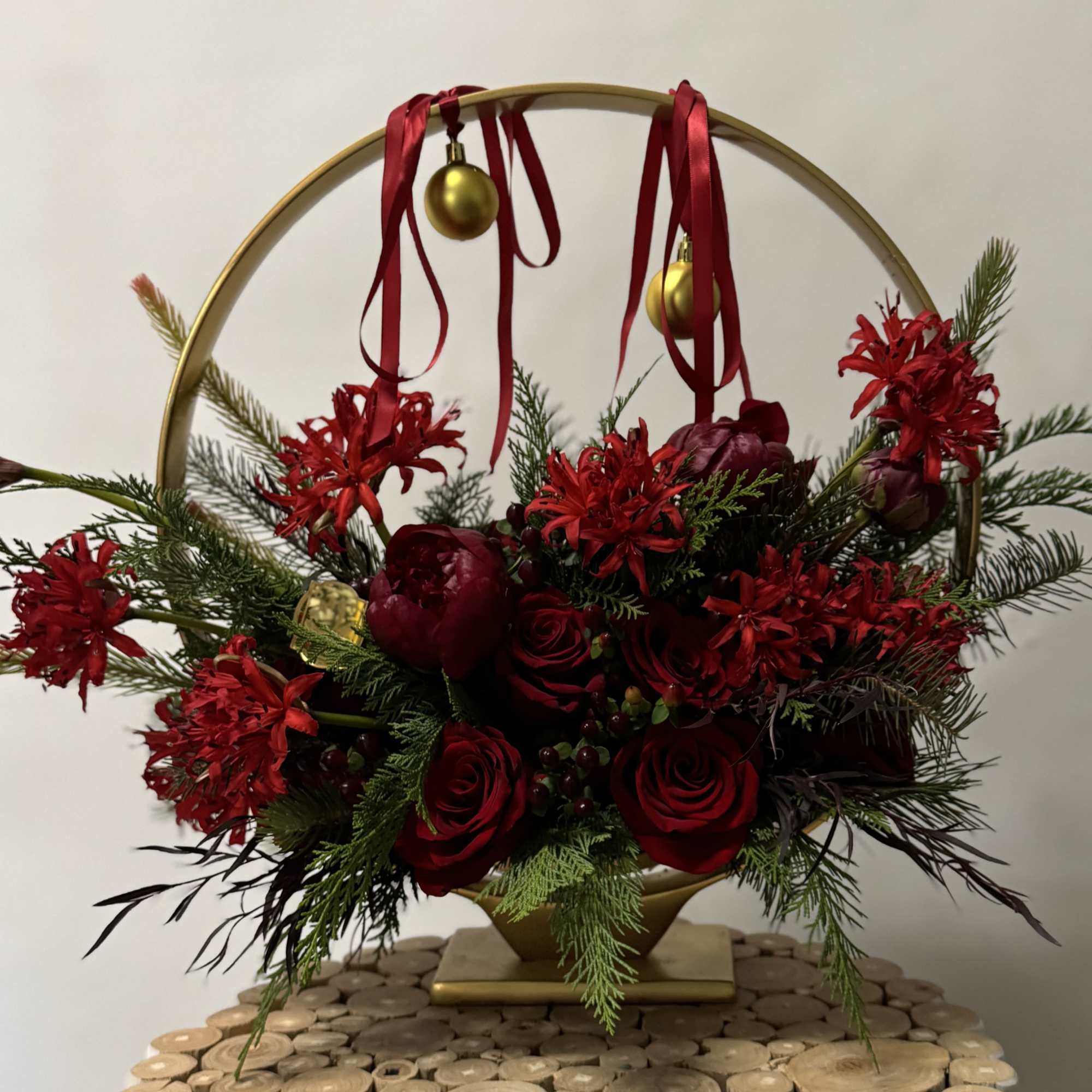 Red roses and holiday flowers arranged in a gold hoop with ribbon and ornaments