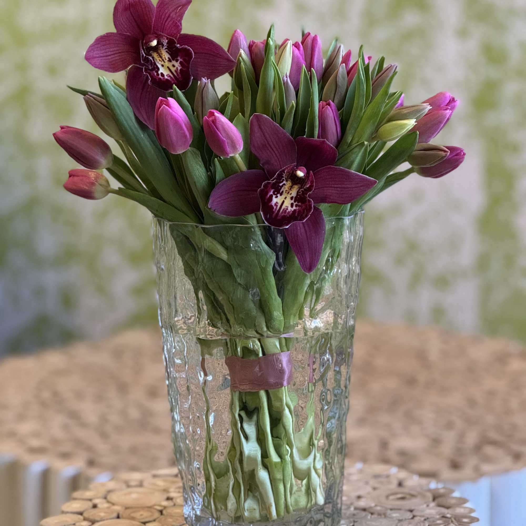 Purple orchids and pink tulips arranged in a clear glass vase