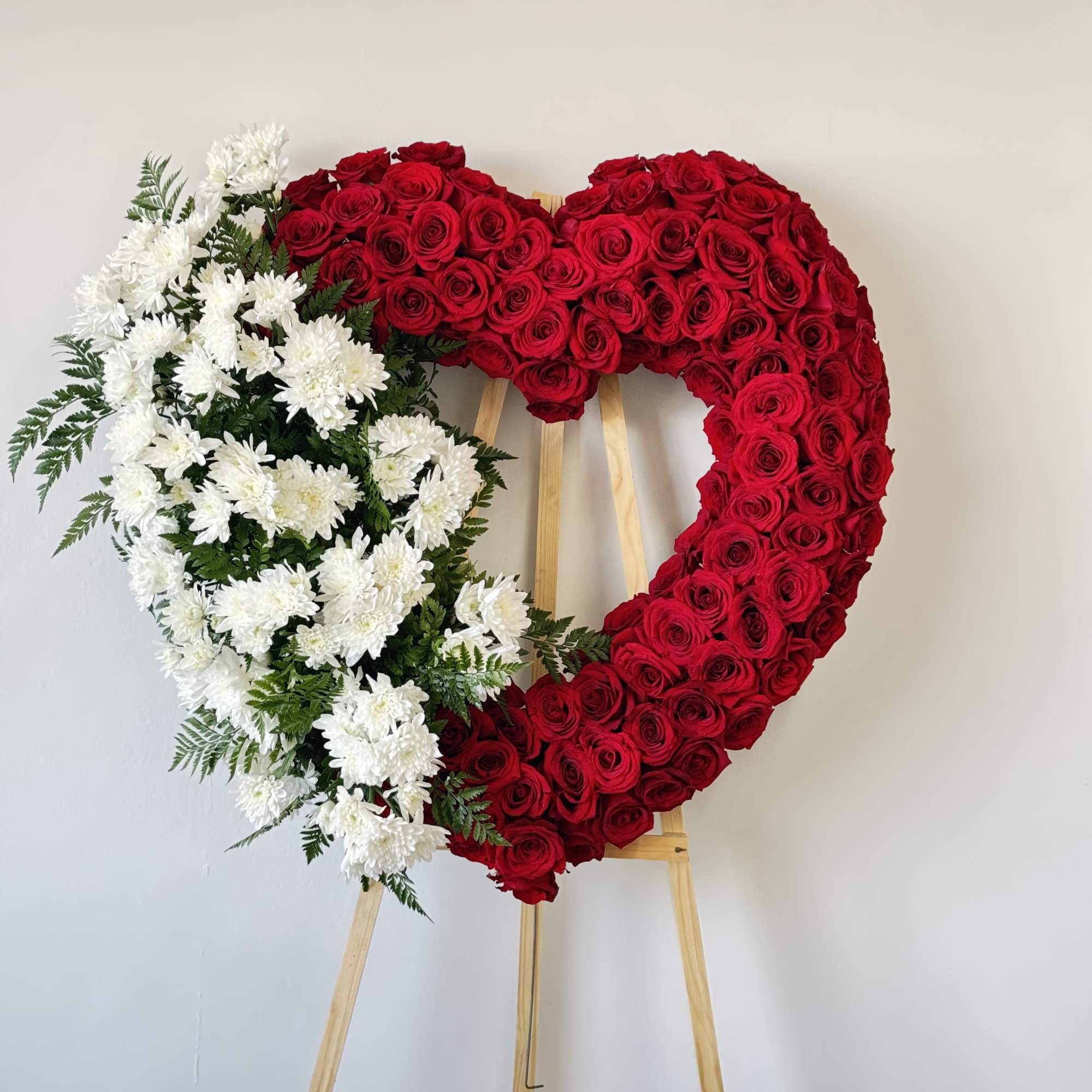 Heart-shaped floral wreath of red roses and white chrysanthemums on an easel
