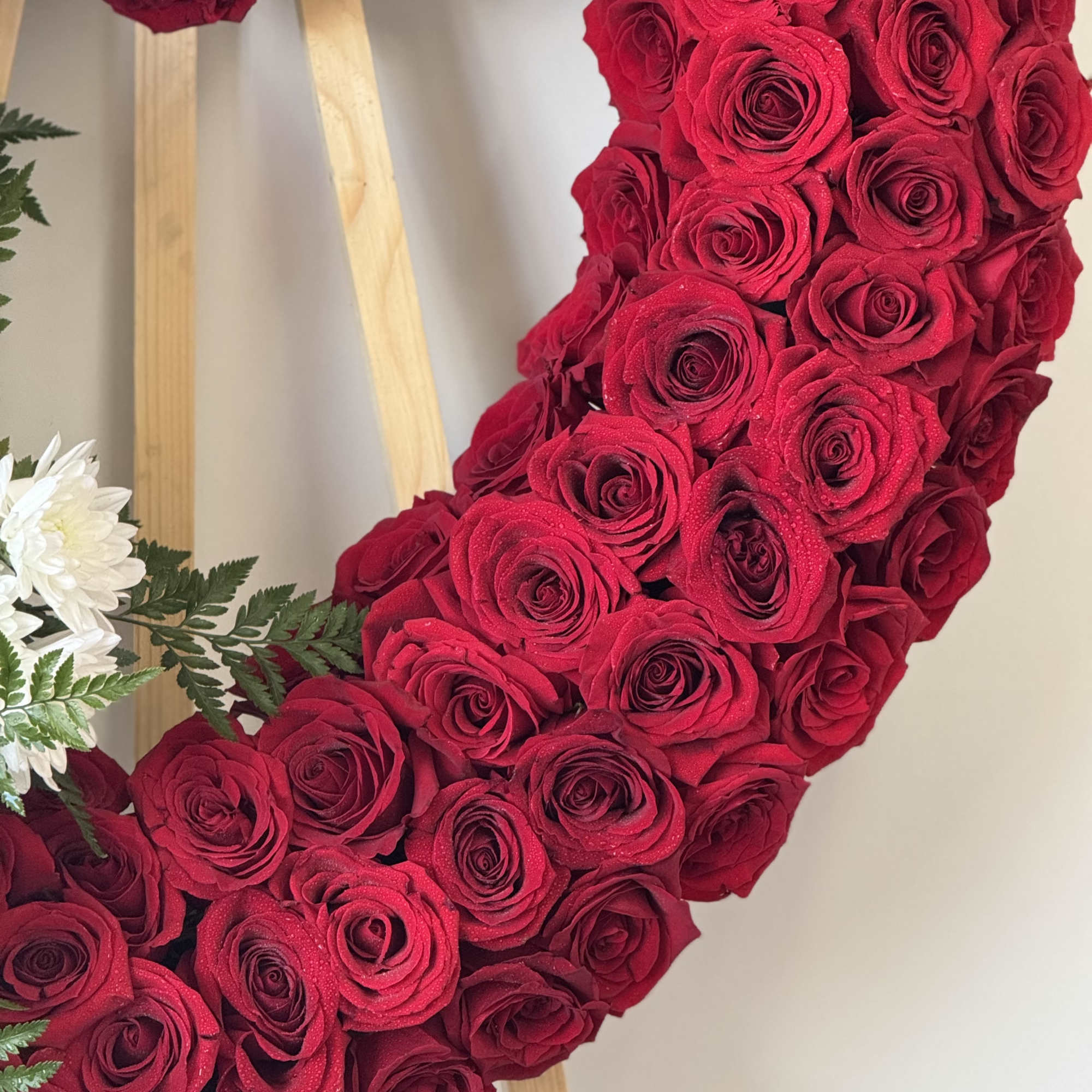 Heart-shaped red rose wreath on a wooden easel with white flowers