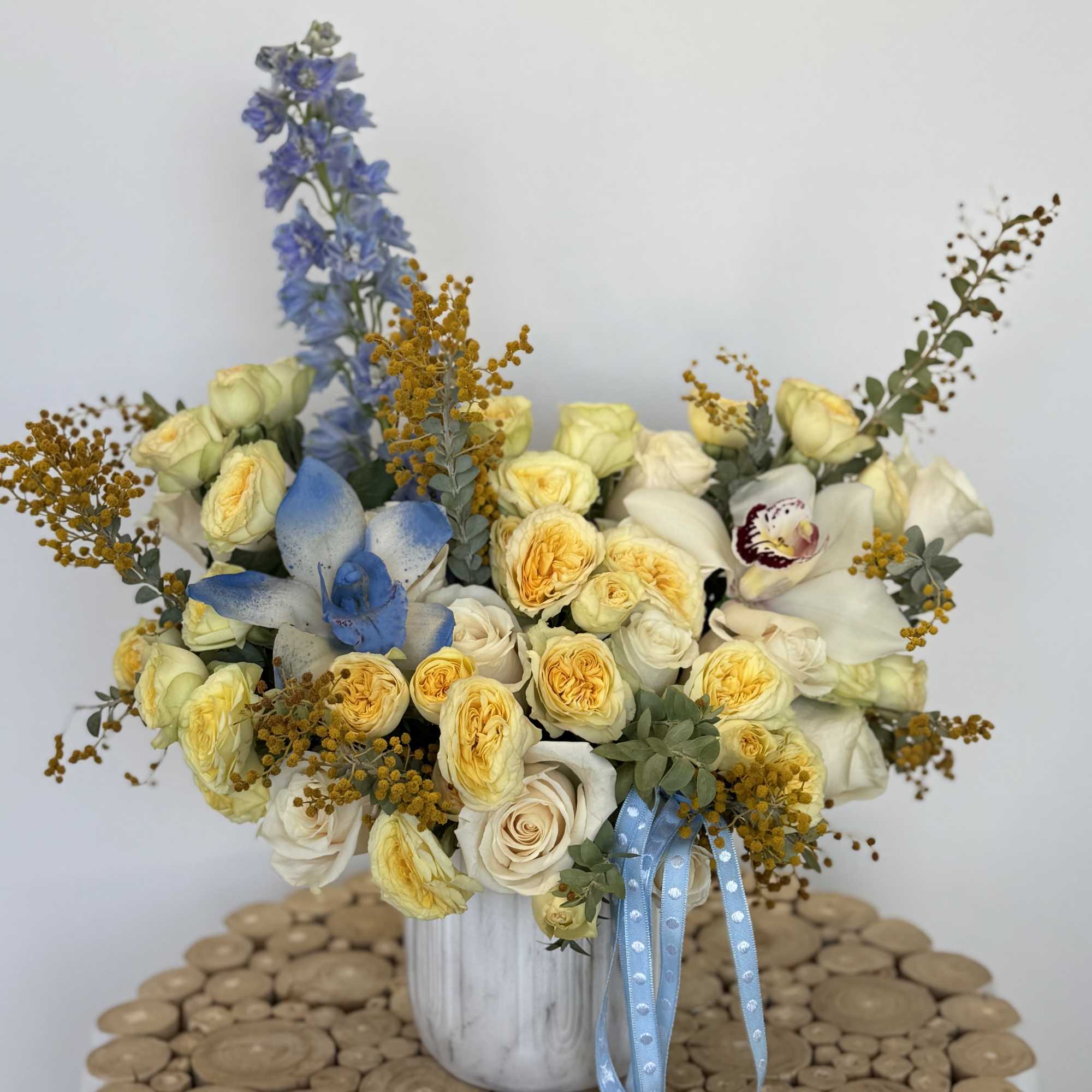 Bouquet of pale yellow and white roses in a white vase with blue ribbon