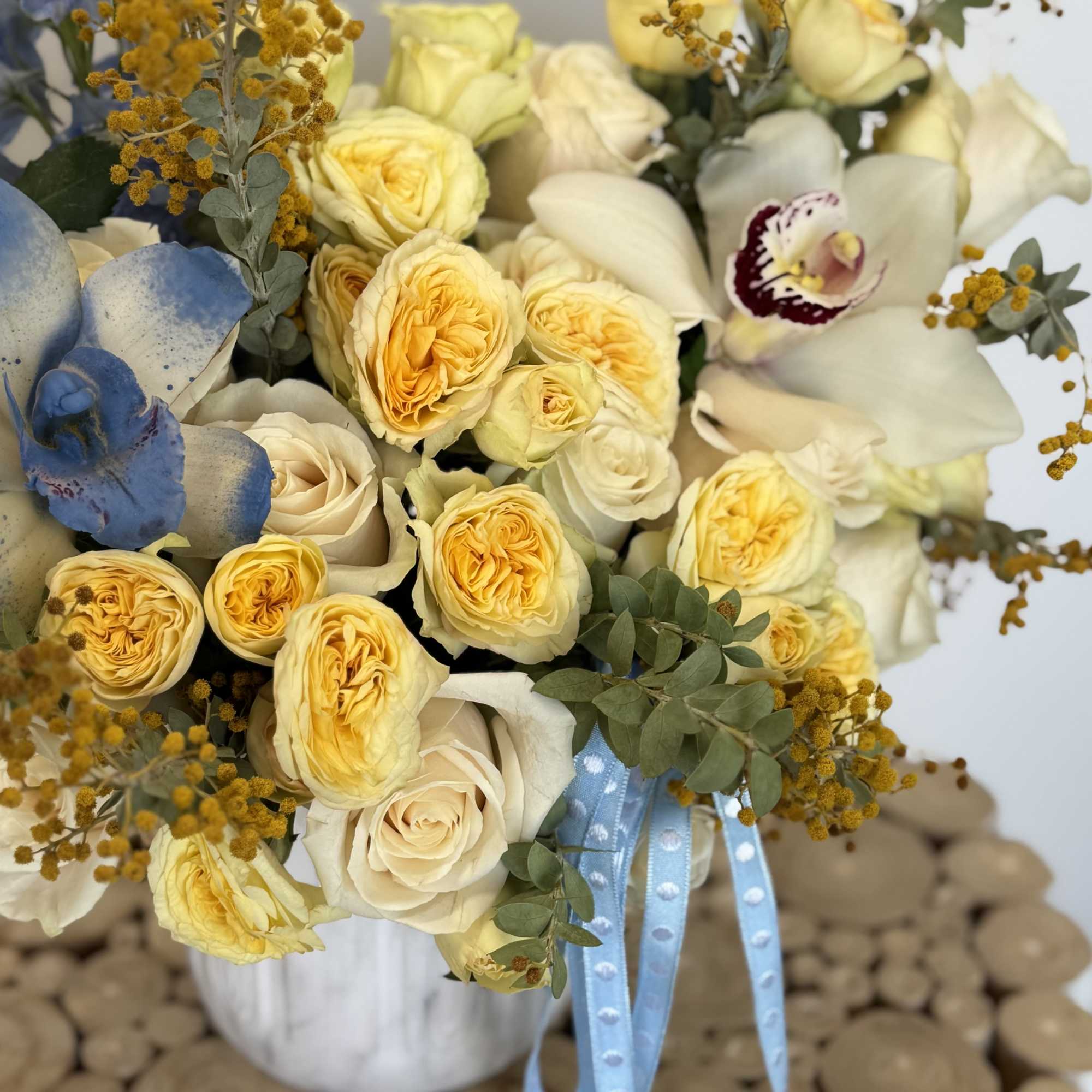 Bouquet of pale yellow roses and white orchids with blue ribbon