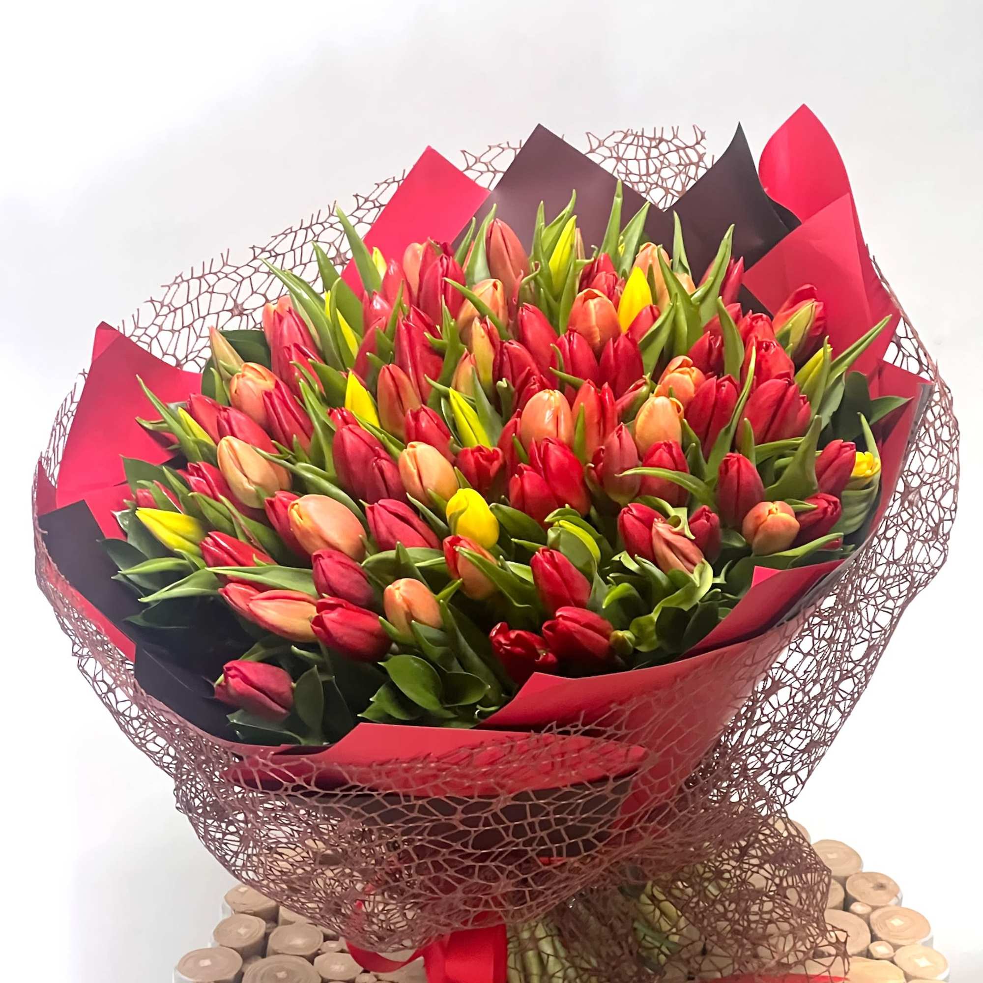 Large bouquet of red, pink, peach, and yellow tulips wrapped in red and black paper