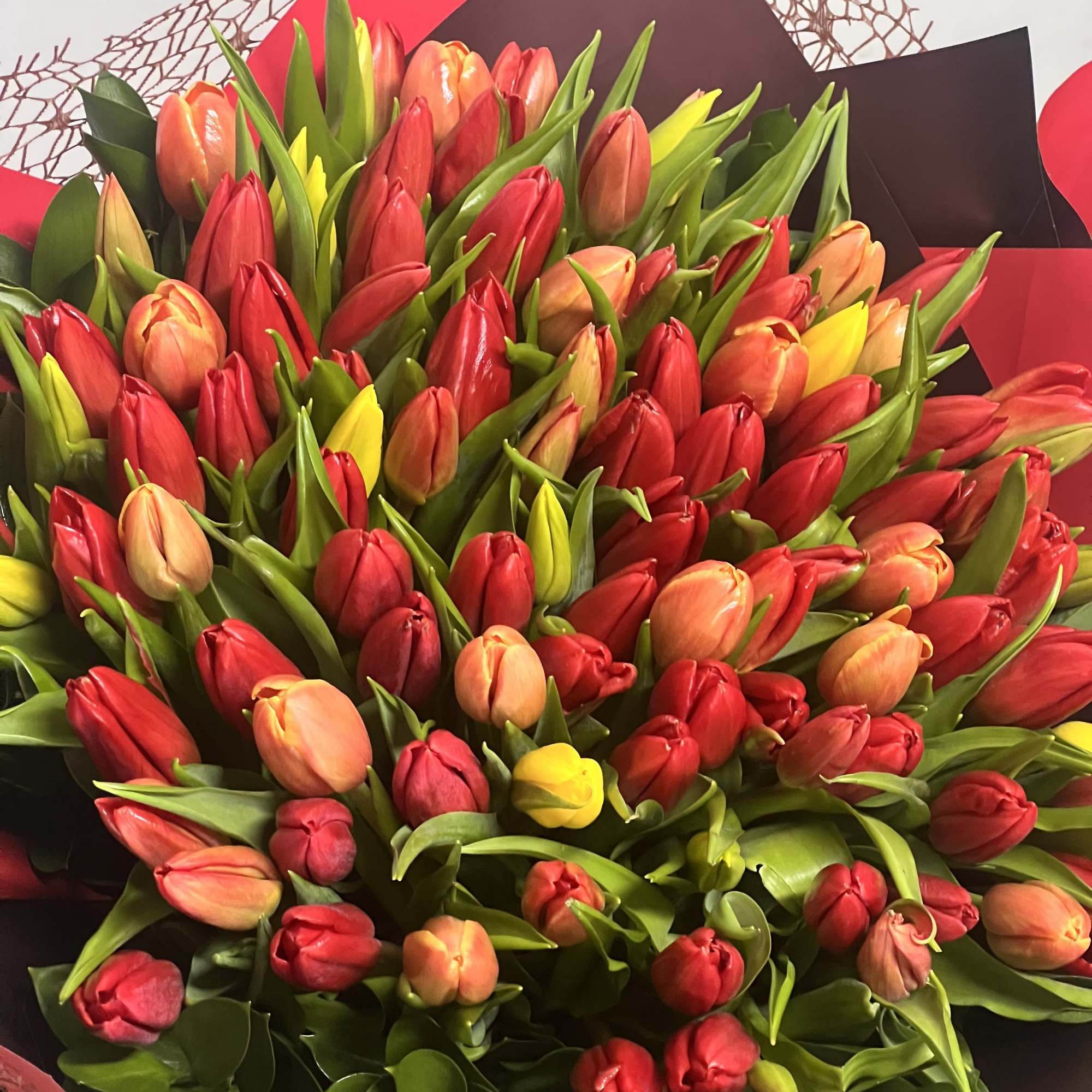 Bouquet of red, peach, and yellow tulips wrapped in black paper