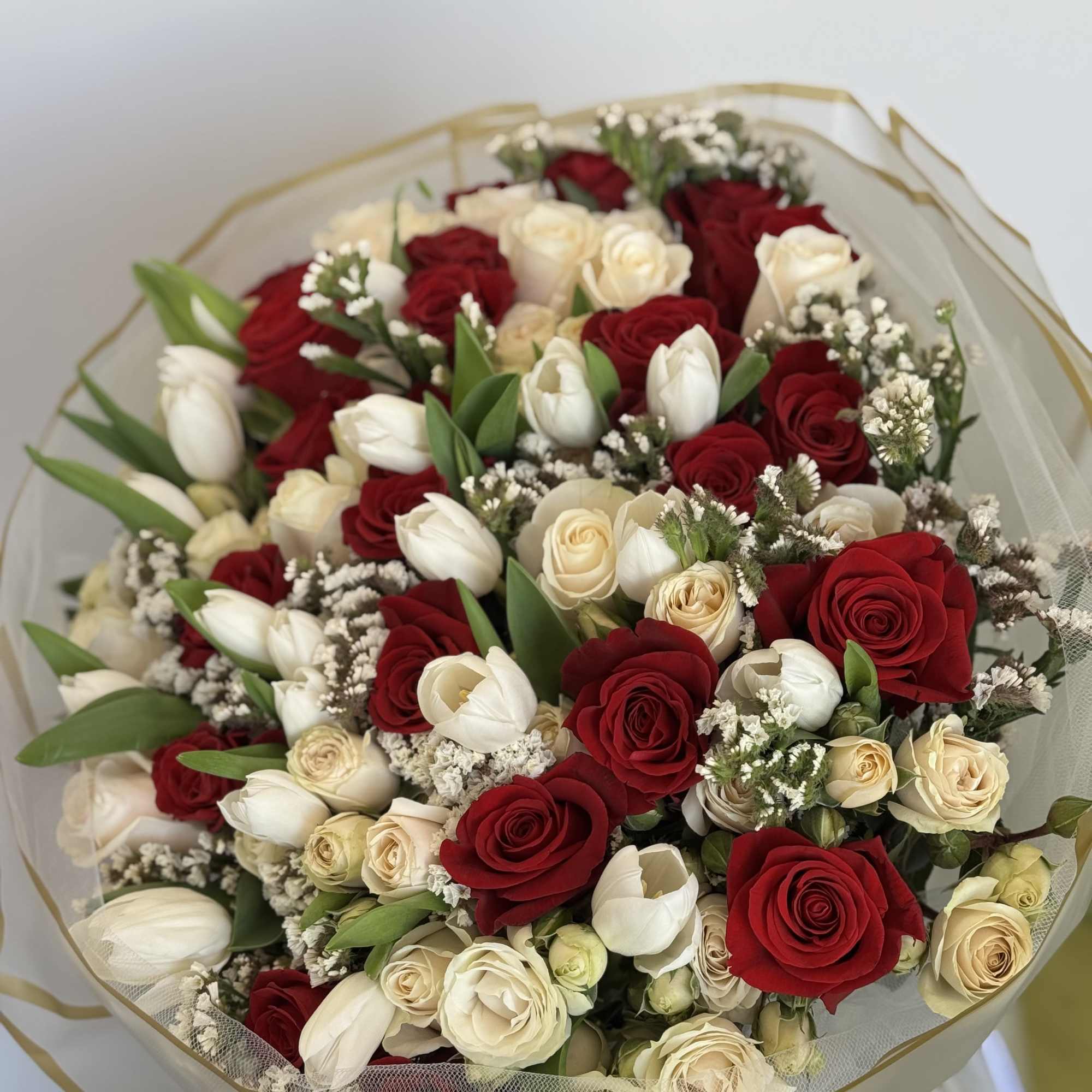 Bouquet of red and cream roses with white tulips wrapped in sheer paper