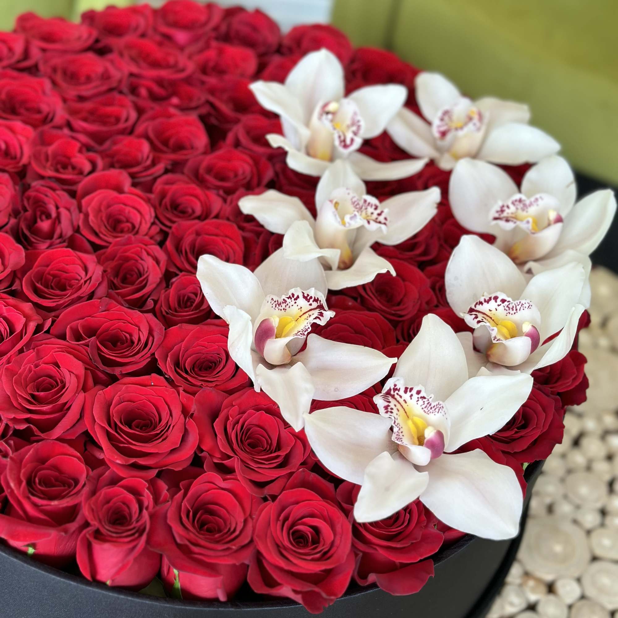 Red roses arranged in a black round box with white orchids on top