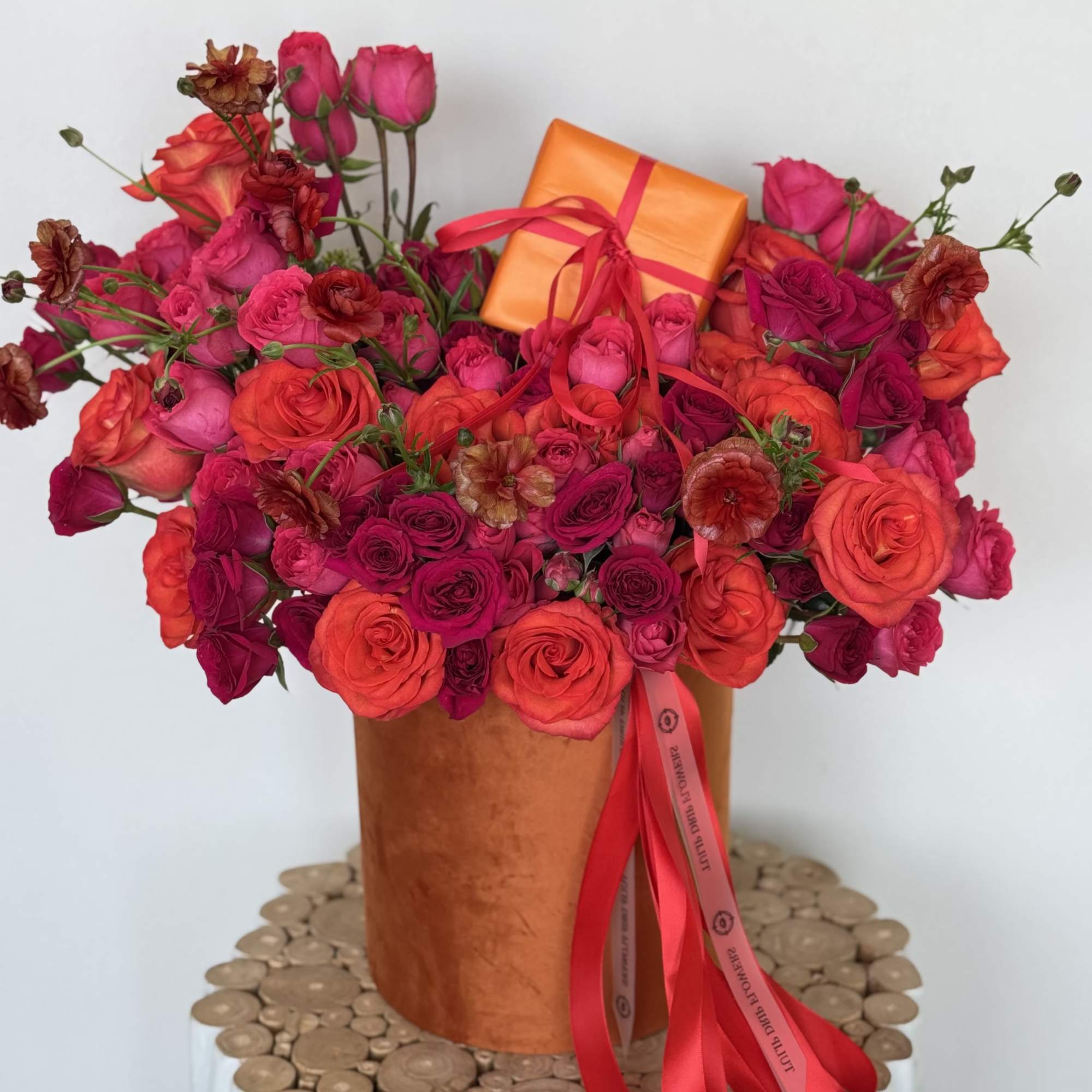 Pink and orange rose bouquet in a copper vase with a small gift box
