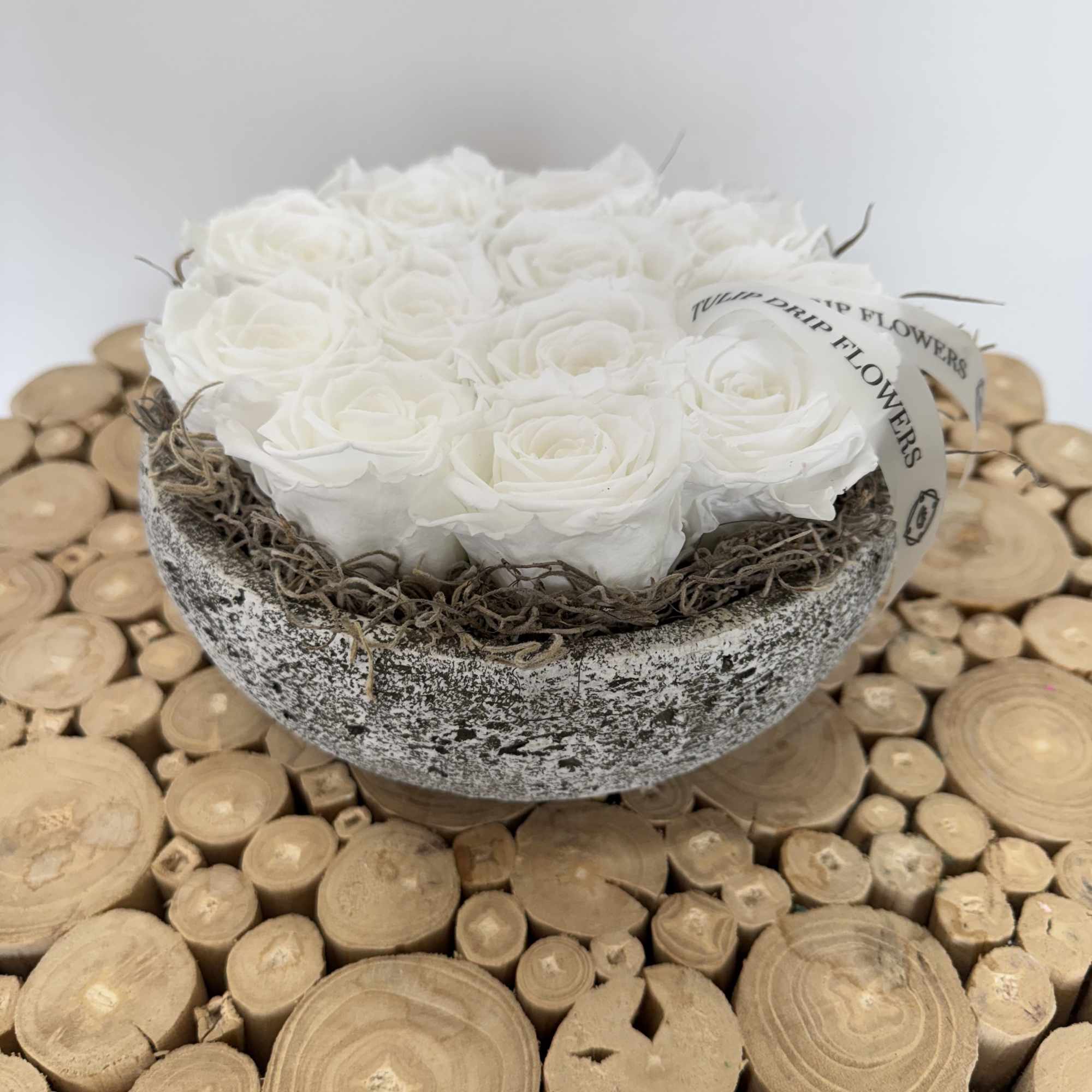 White roses arranged in a rustic bowl on a wood-slice surface