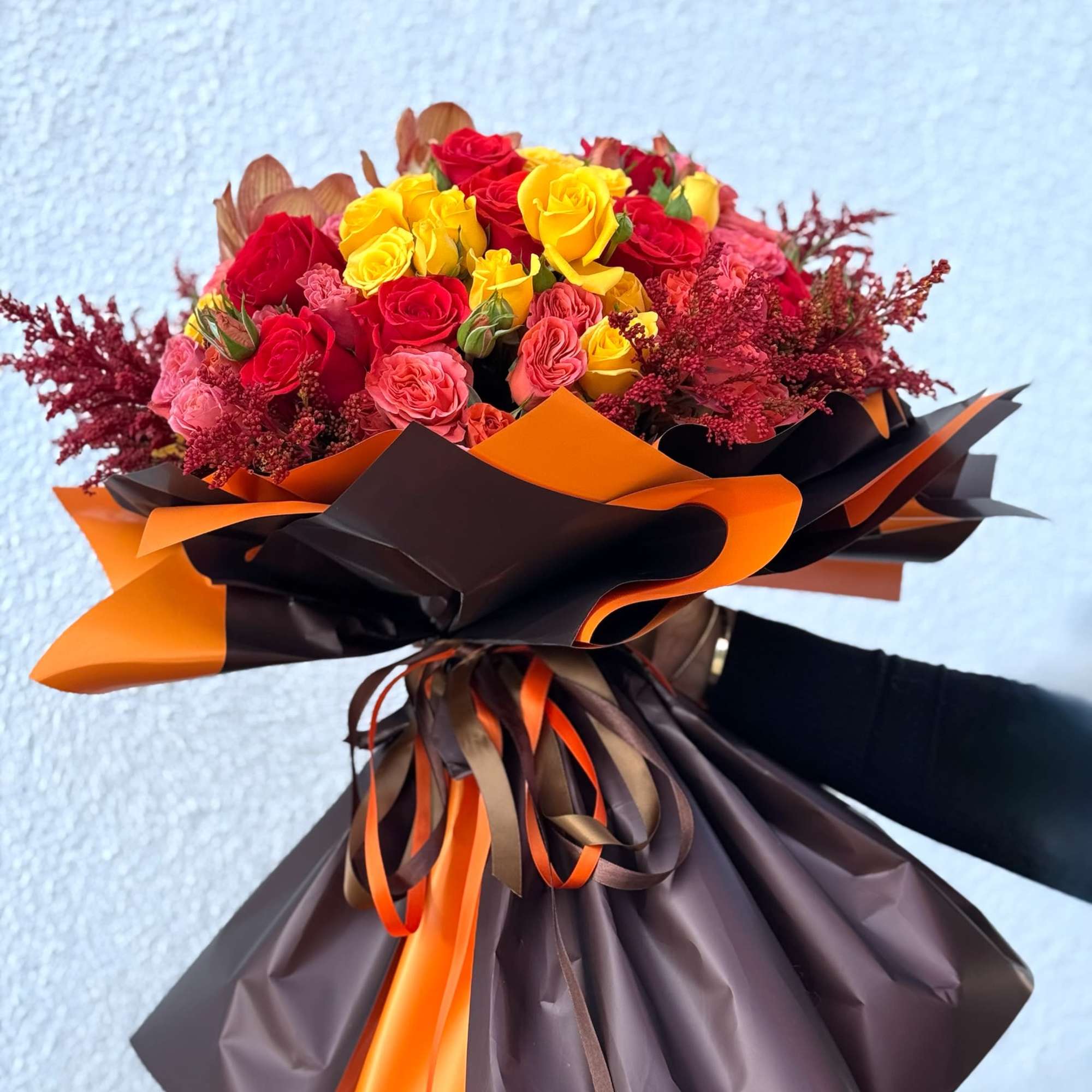 Bouquet of red, yellow, and pink roses wrapped in orange and brown paper
