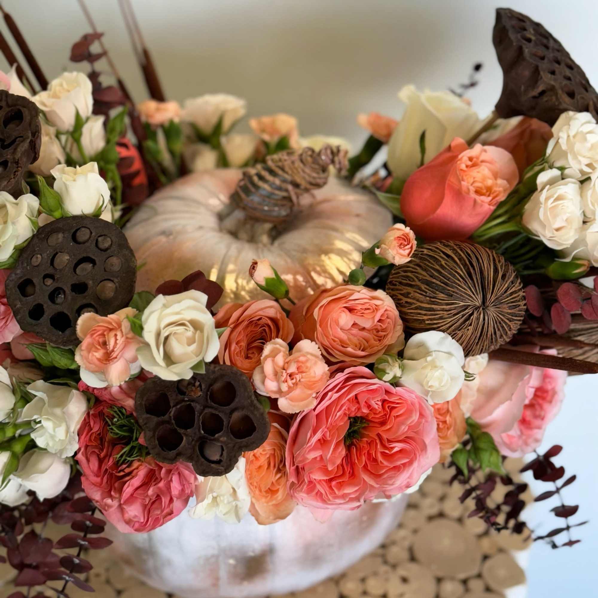 Mixed pink and white roses arranged around a pale pumpkin centerpiece