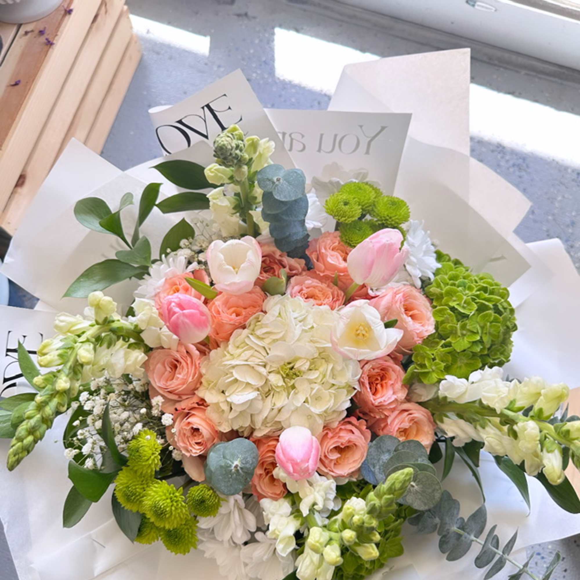 Bouquet of pink roses, white hydrangea, and tulips wrapped in white paper