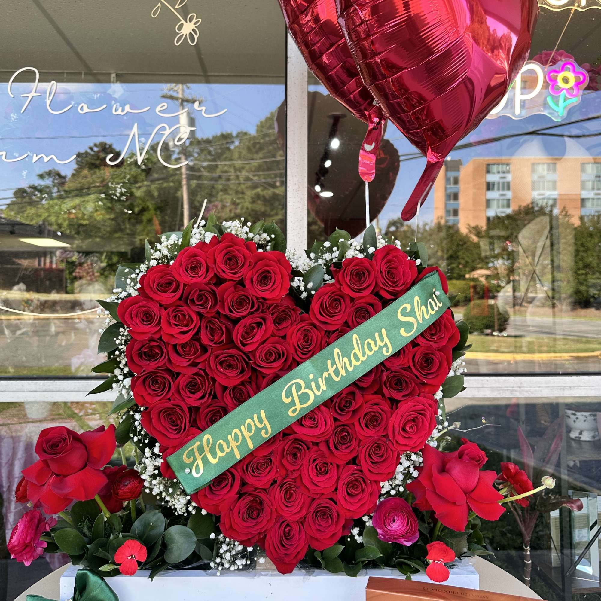 Heart-shaped red rose arrangement with a birthday sash and heart balloons