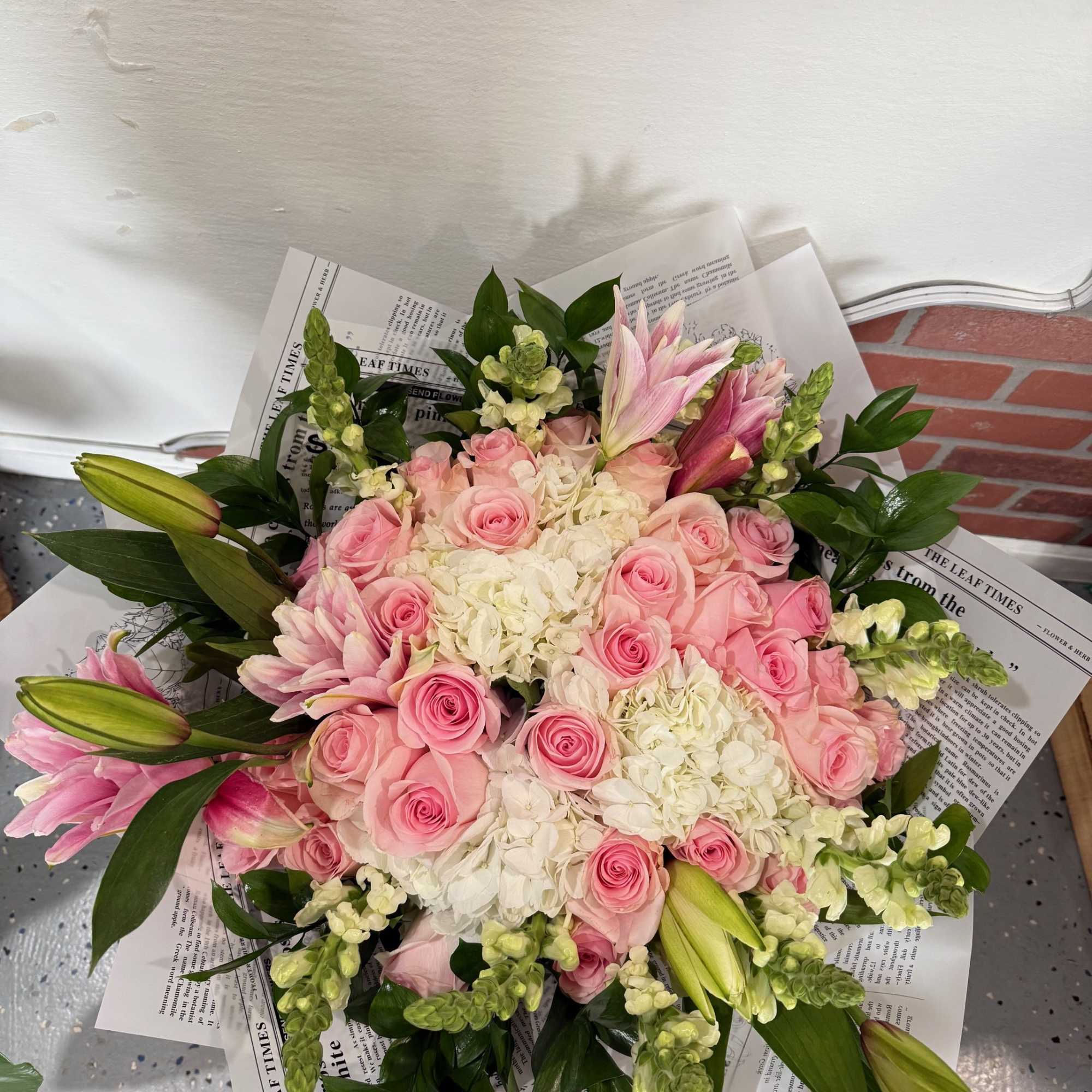 Pink roses and lilies arranged with white hydrangeas in newspaper wrap