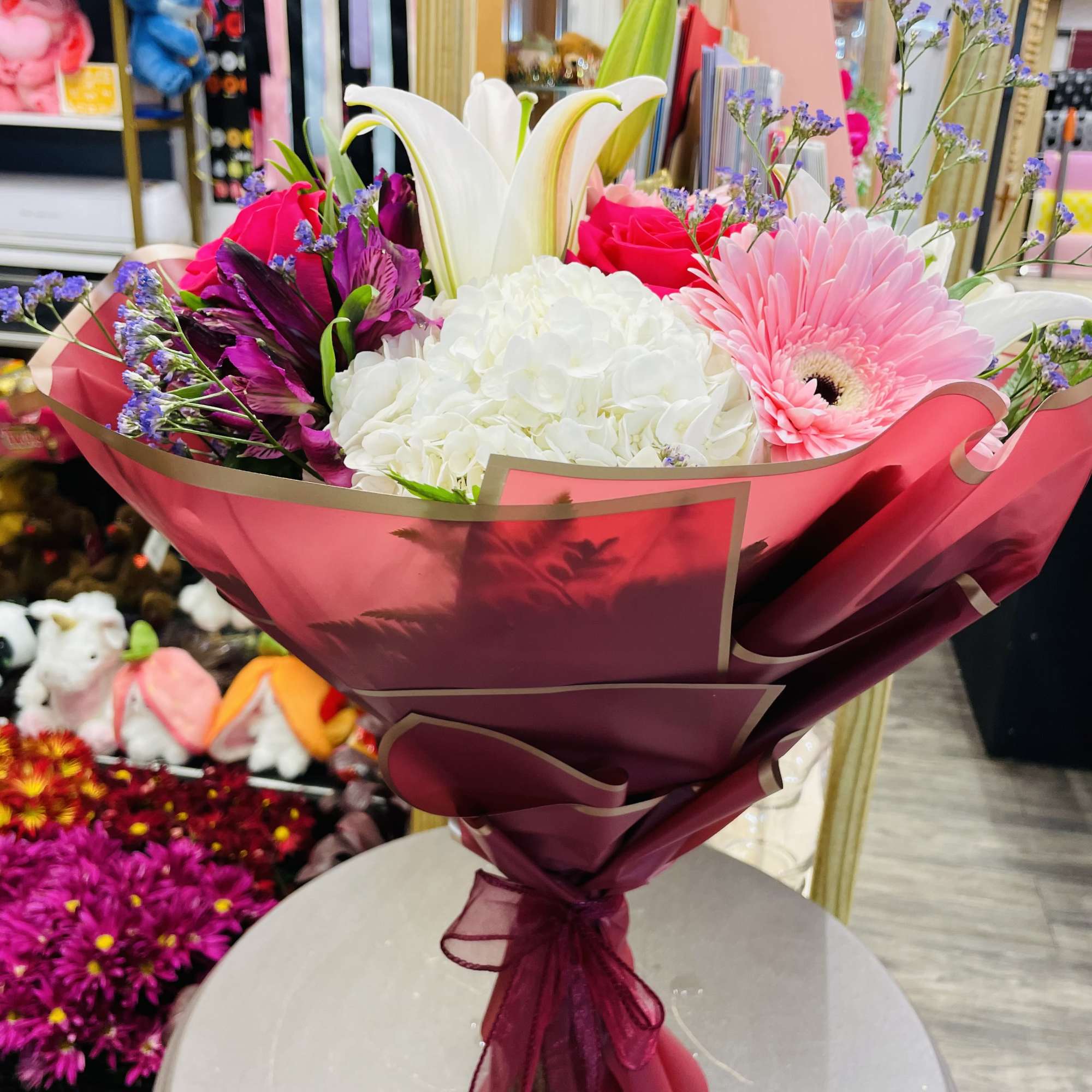 Bouquet of lilies, roses, hydrangea, and a pink gerbera daisy in magenta wrap