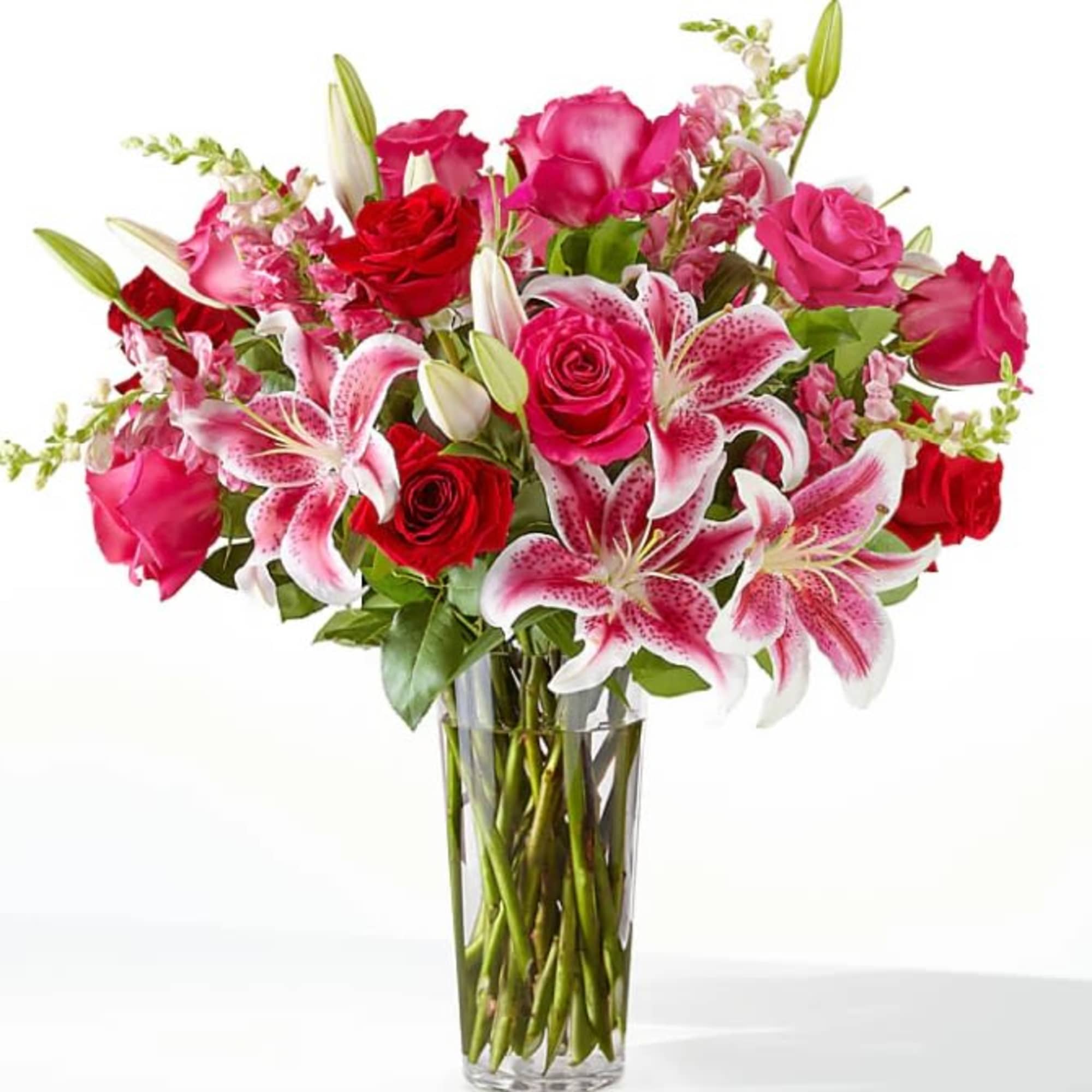 Tall bouquet of pink lilies and red and pink roses in a clear glass vase
