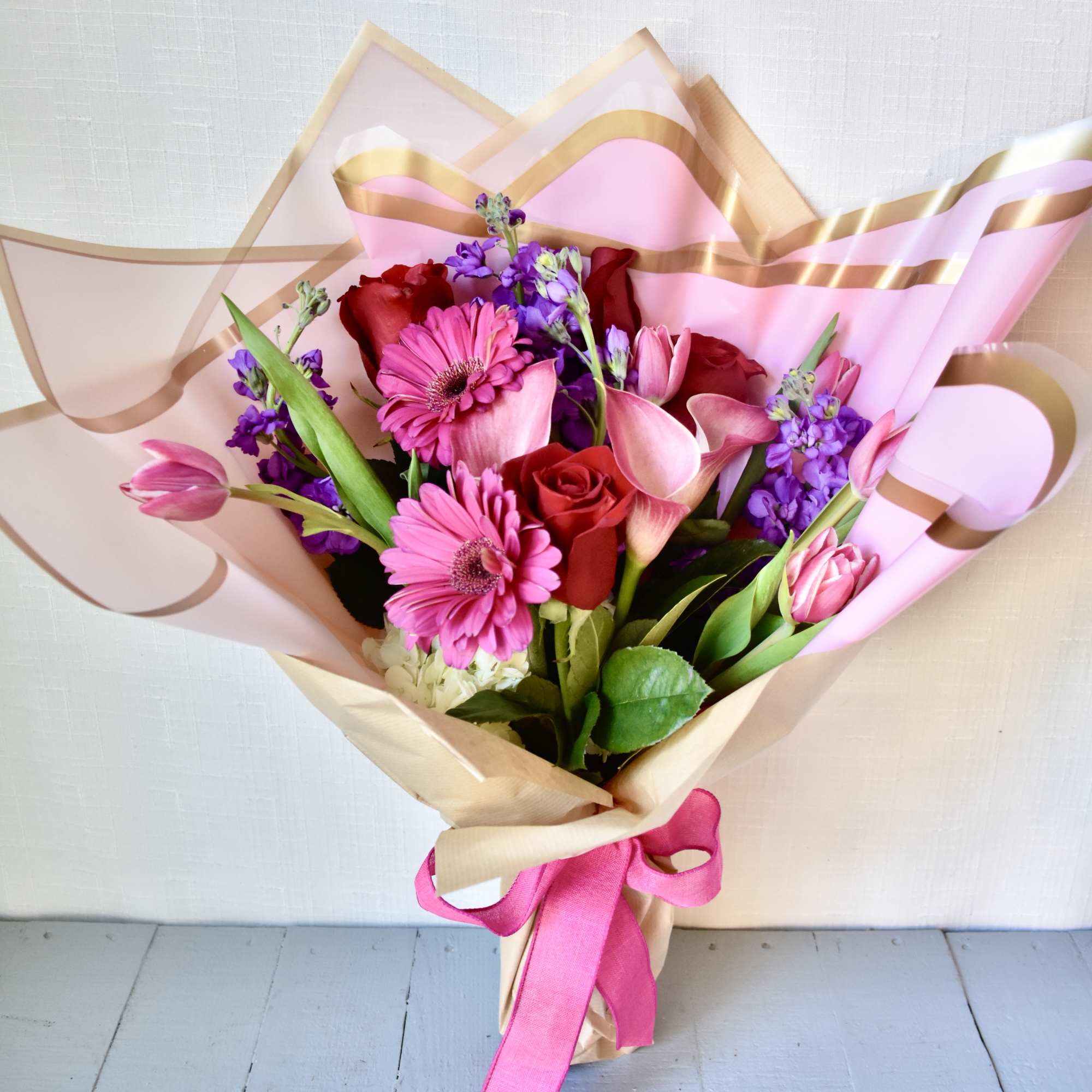 Bouquet of pink gerbera daisies, red roses, and purple flowers wrapped in pink paper