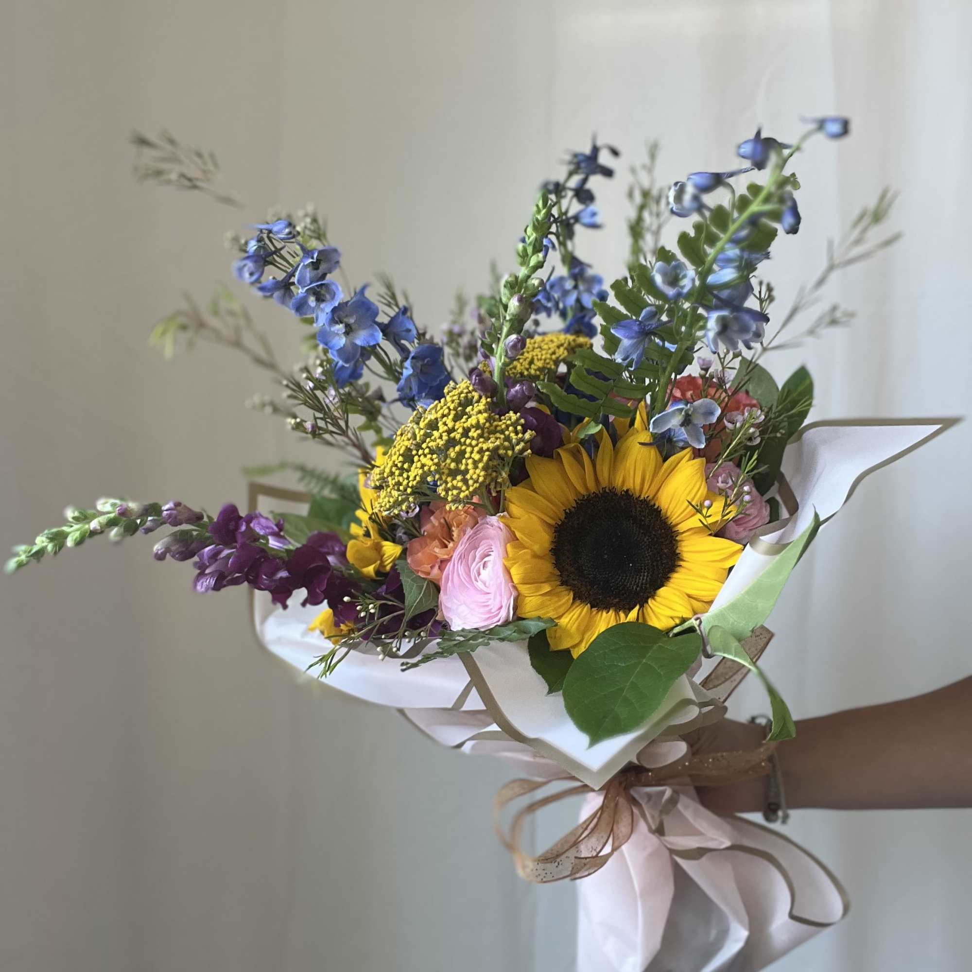 Hand-tied bouquet with a sunflower, blue flowers, and pink blooms