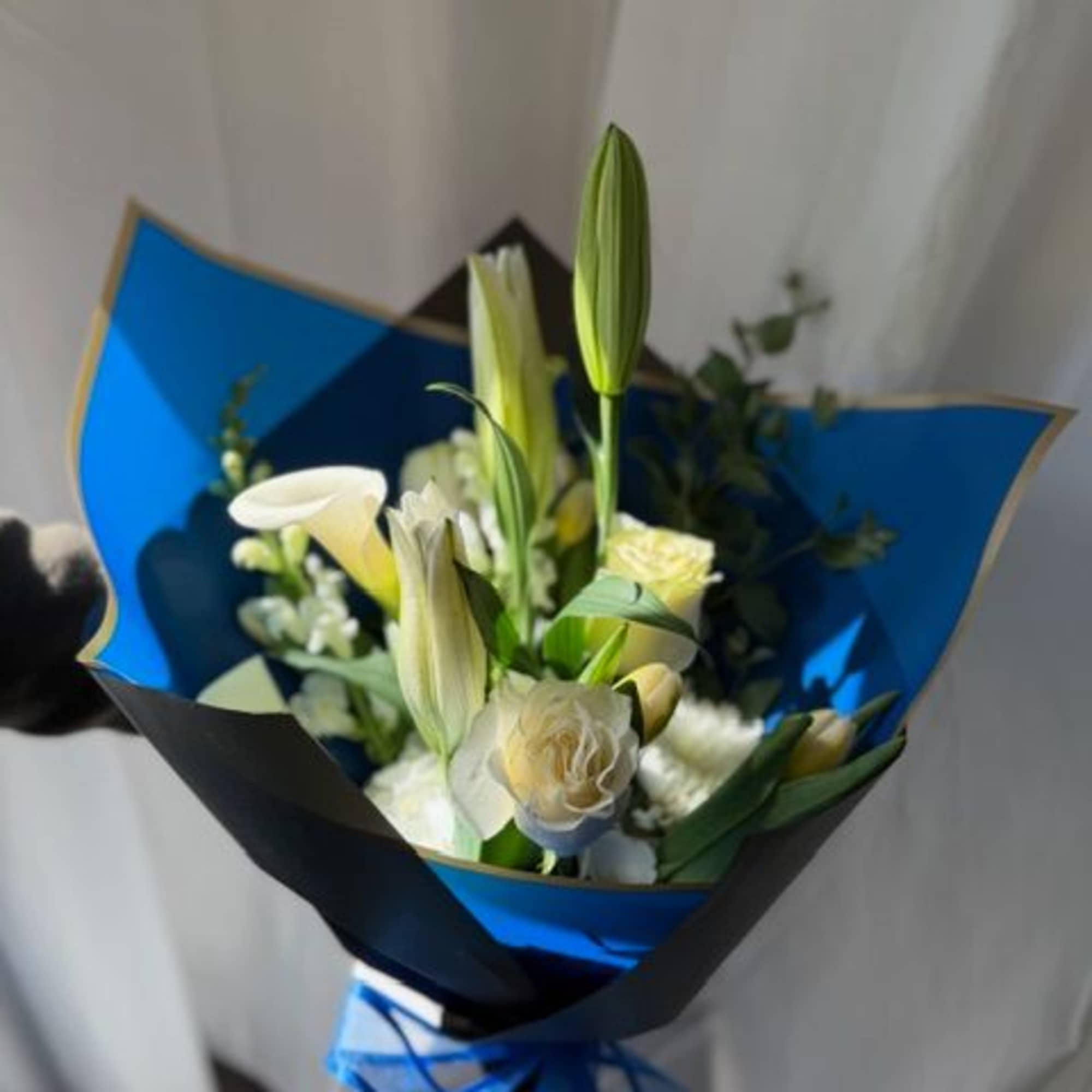 Bouquet of white lilies and pale roses wrapped in blue paper