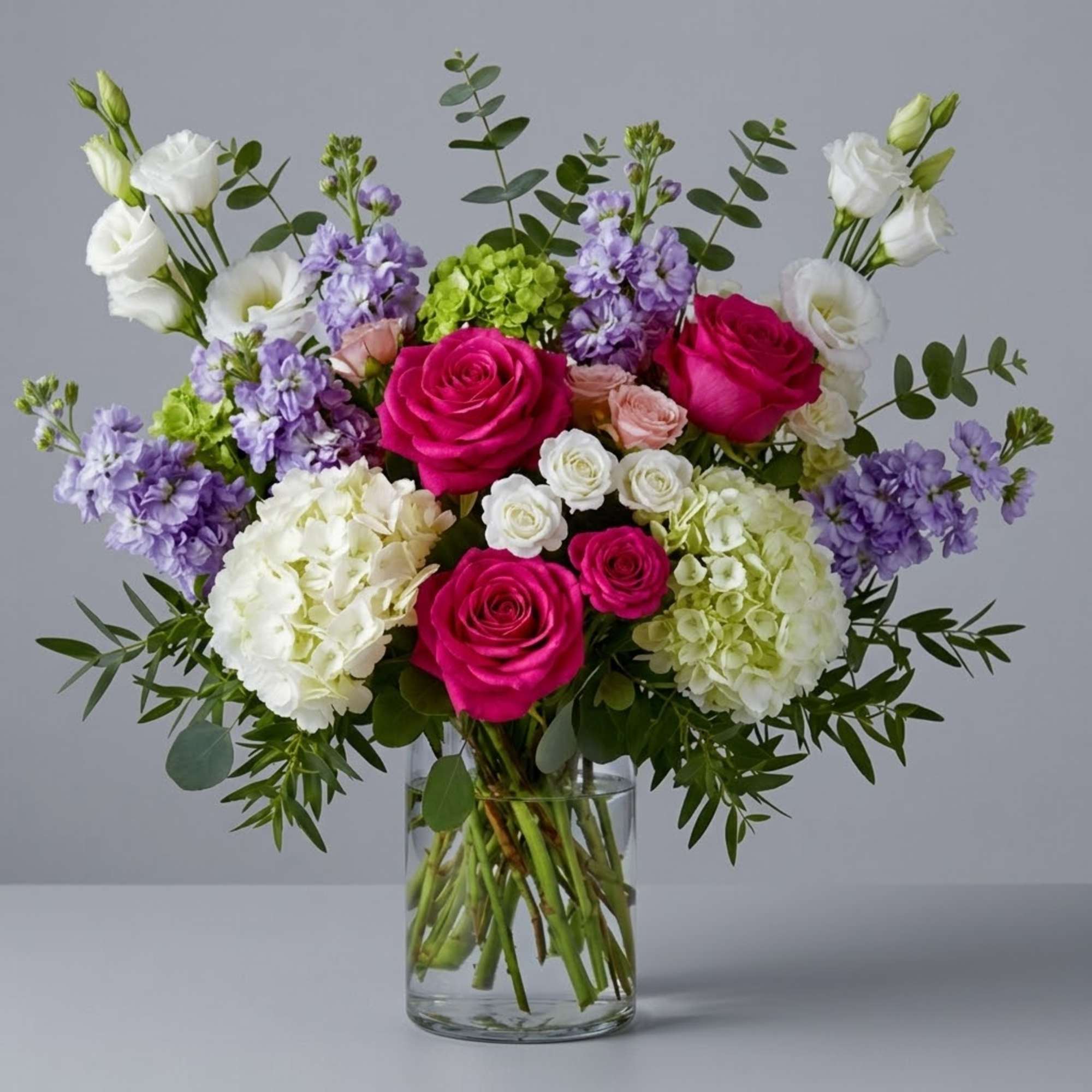 Bouquet of pink roses, white lisianthus, and purple flowers in a glass vase