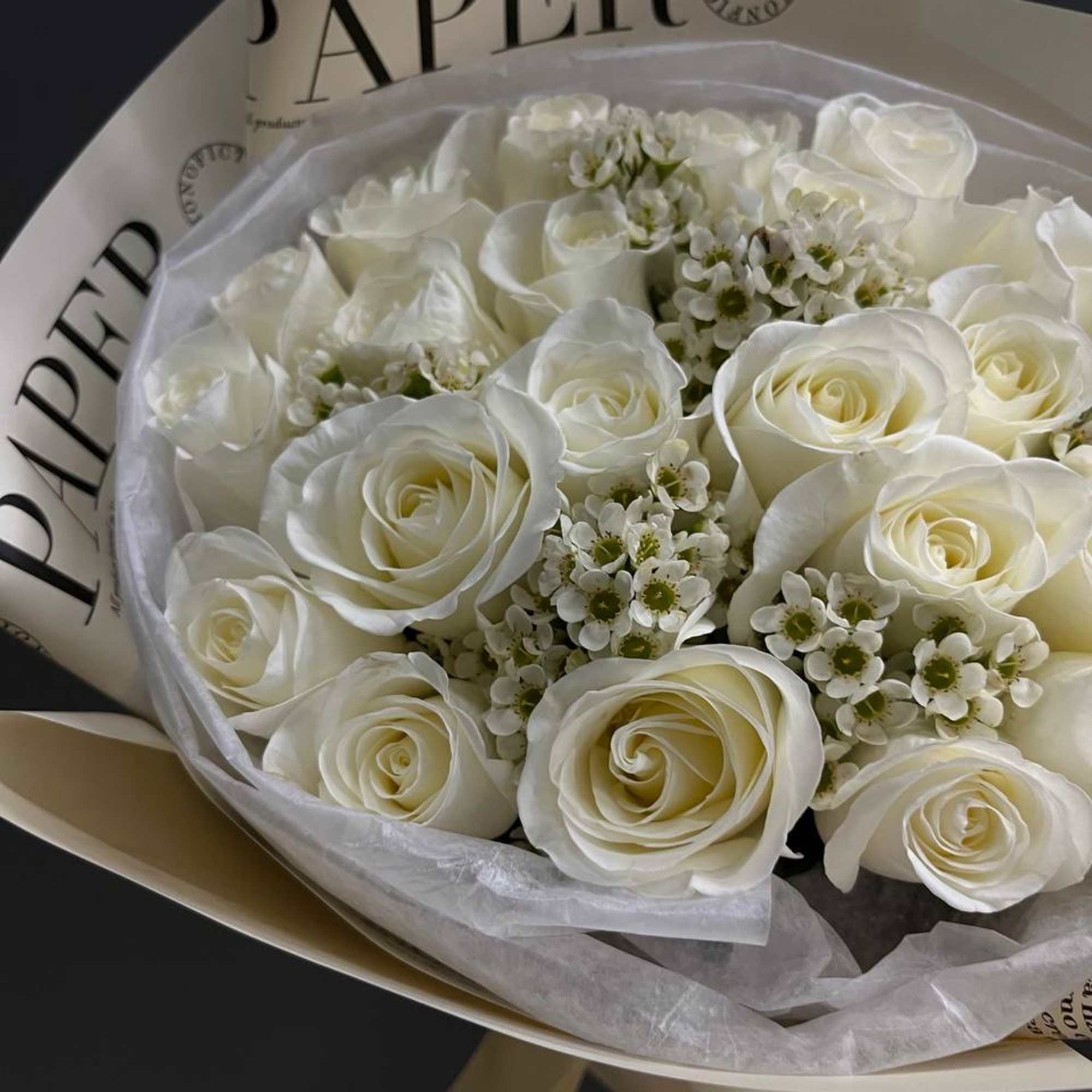 Bouquet of white roses with small white filler flowers wrapped in paper