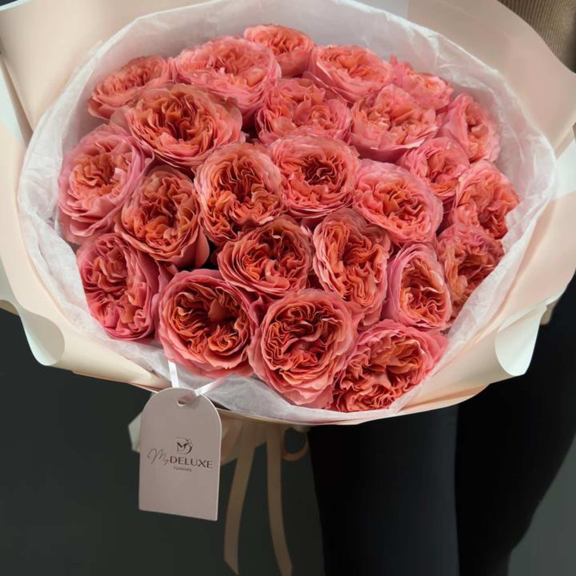 Large bouquet of coral-pink roses wrapped in pale paper