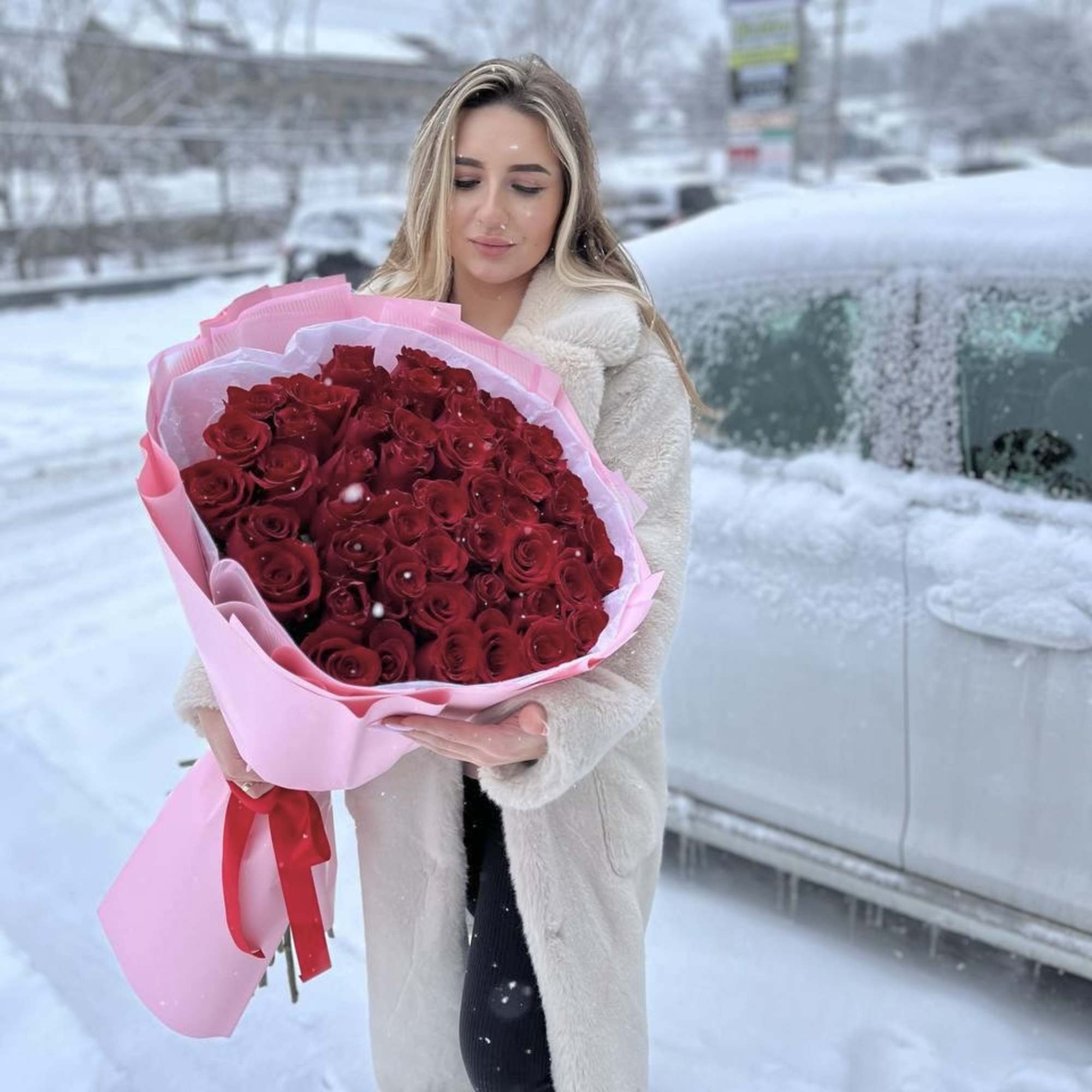 Woman holding a large bouquet of red roses wrapped in pink paper
