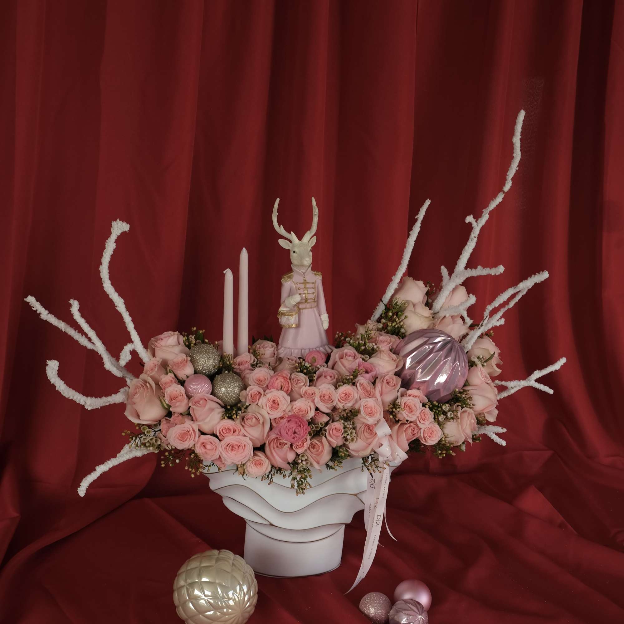 Pink rose arrangement in a white vase with decorative ornaments and a small figurine