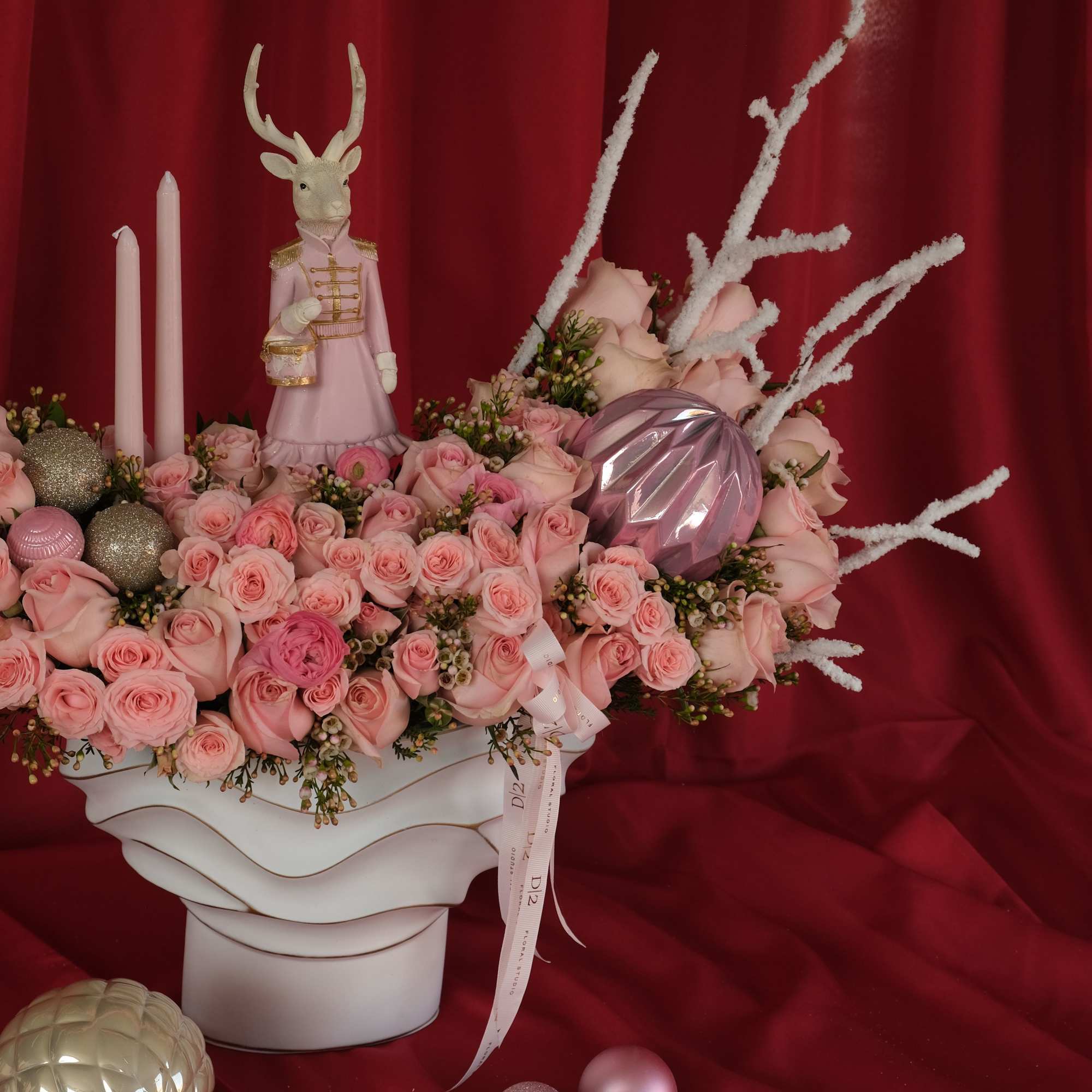 Pink rose arrangement with candles and a deer figurine in a white vase