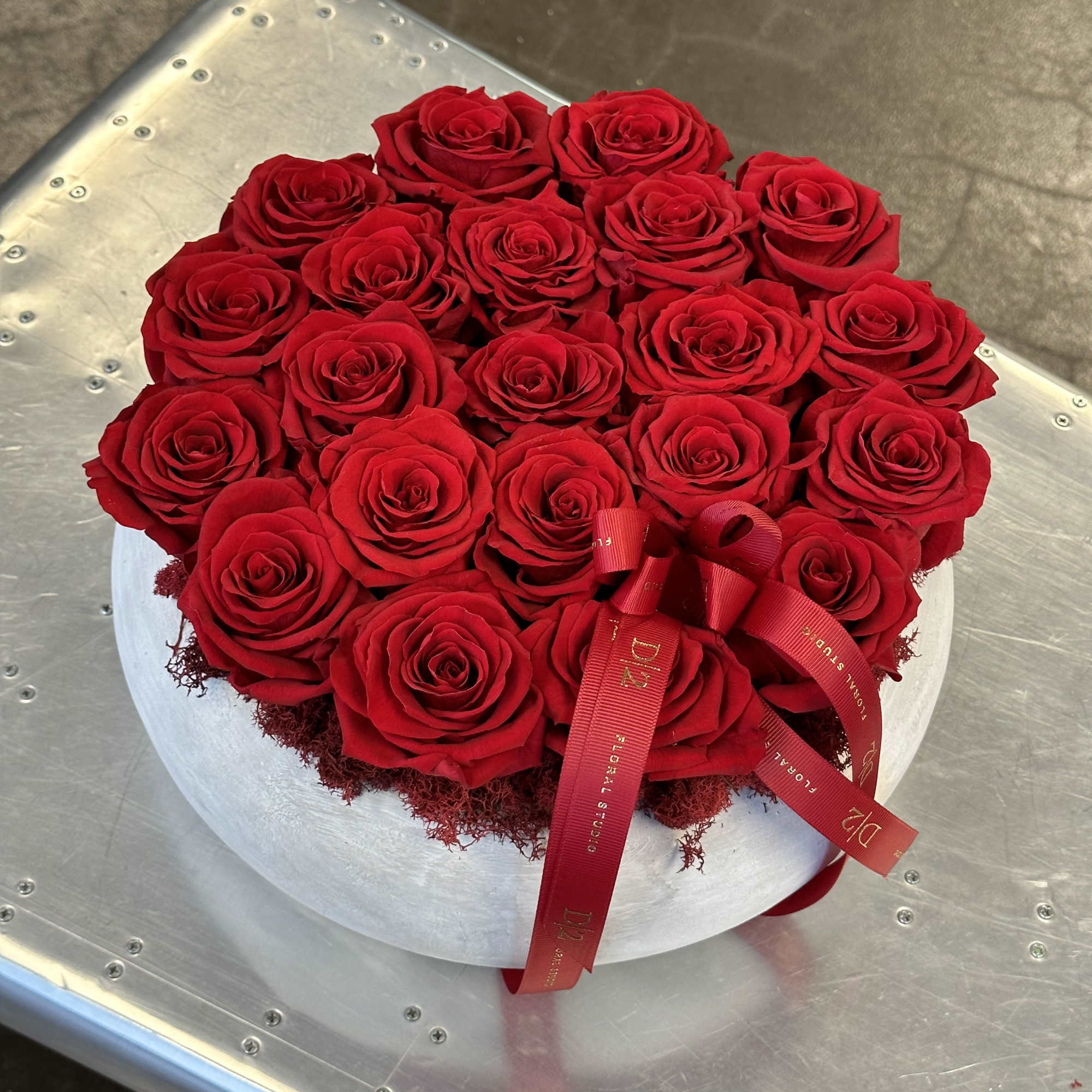 Round arrangement of red roses in a white hat box with a red ribbon